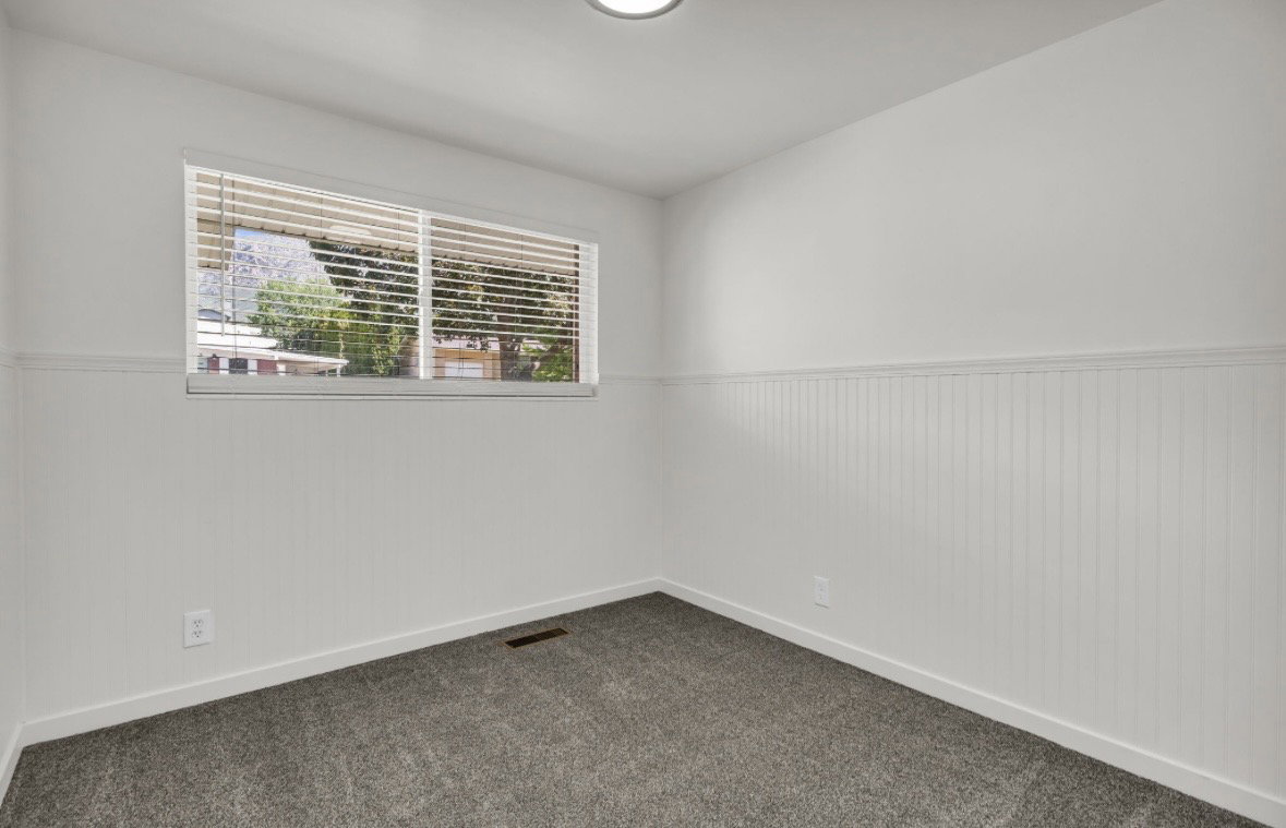 Room featuring beadboard wainscoting, white walls, and a window with horizontal blinds
