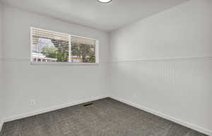 Room featuring beadboard wainscoting, white walls, and a window with horizontal blinds