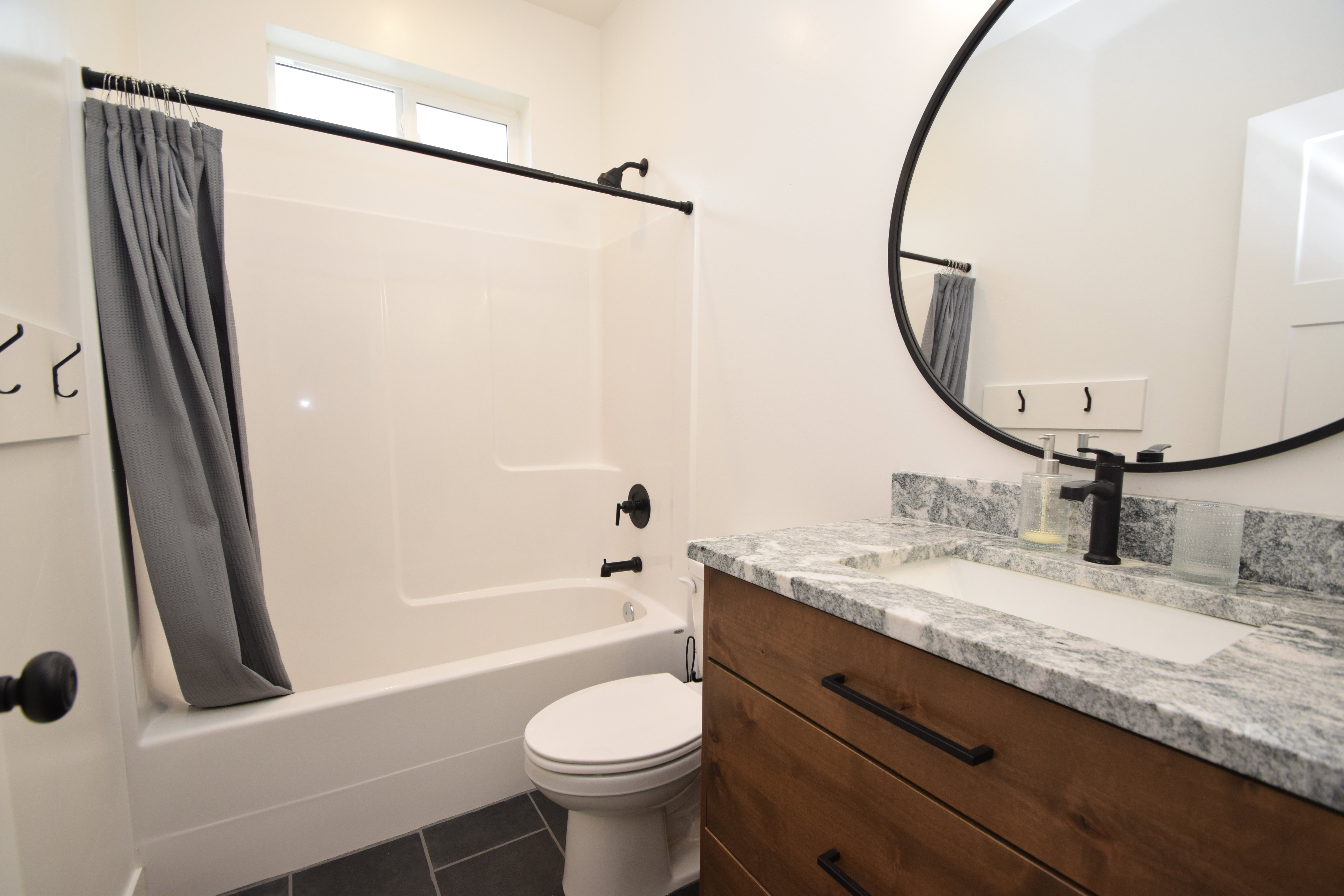 Bathroom featuring a white tub and shower combination with black fixtures, a white toilet, and dark tile flooring