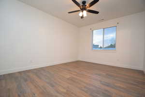 Room featuring wood-finish flooring, white walls, a large window with blinds, and a ceiling fan with integrated lighting
