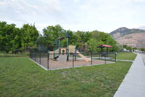 Fenced playground area featuring a play structure with slide, a separate covered picnic area, and surrounding green space
