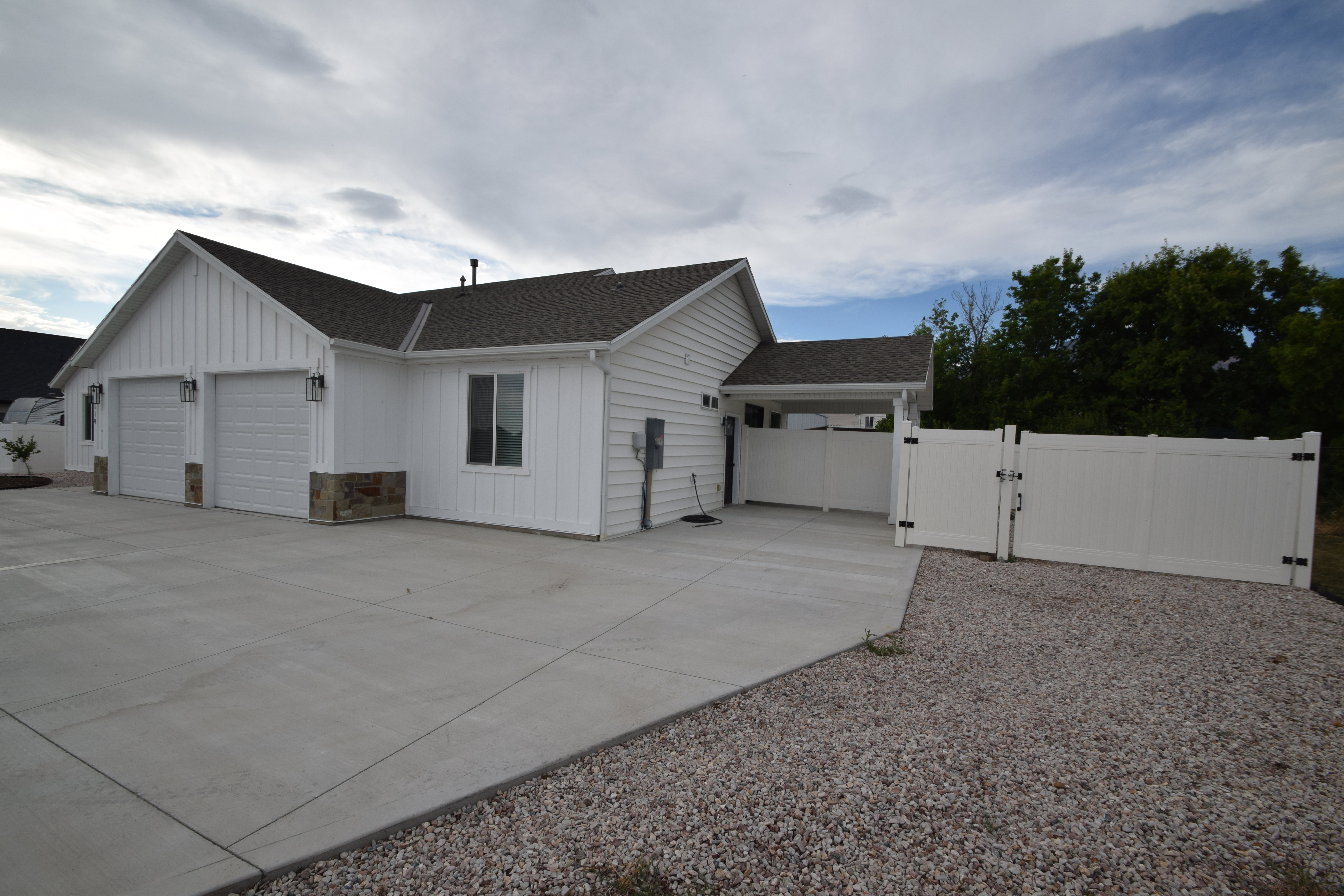 White board and batten exterior with a two-car garage, stone accents, and a covered patio area