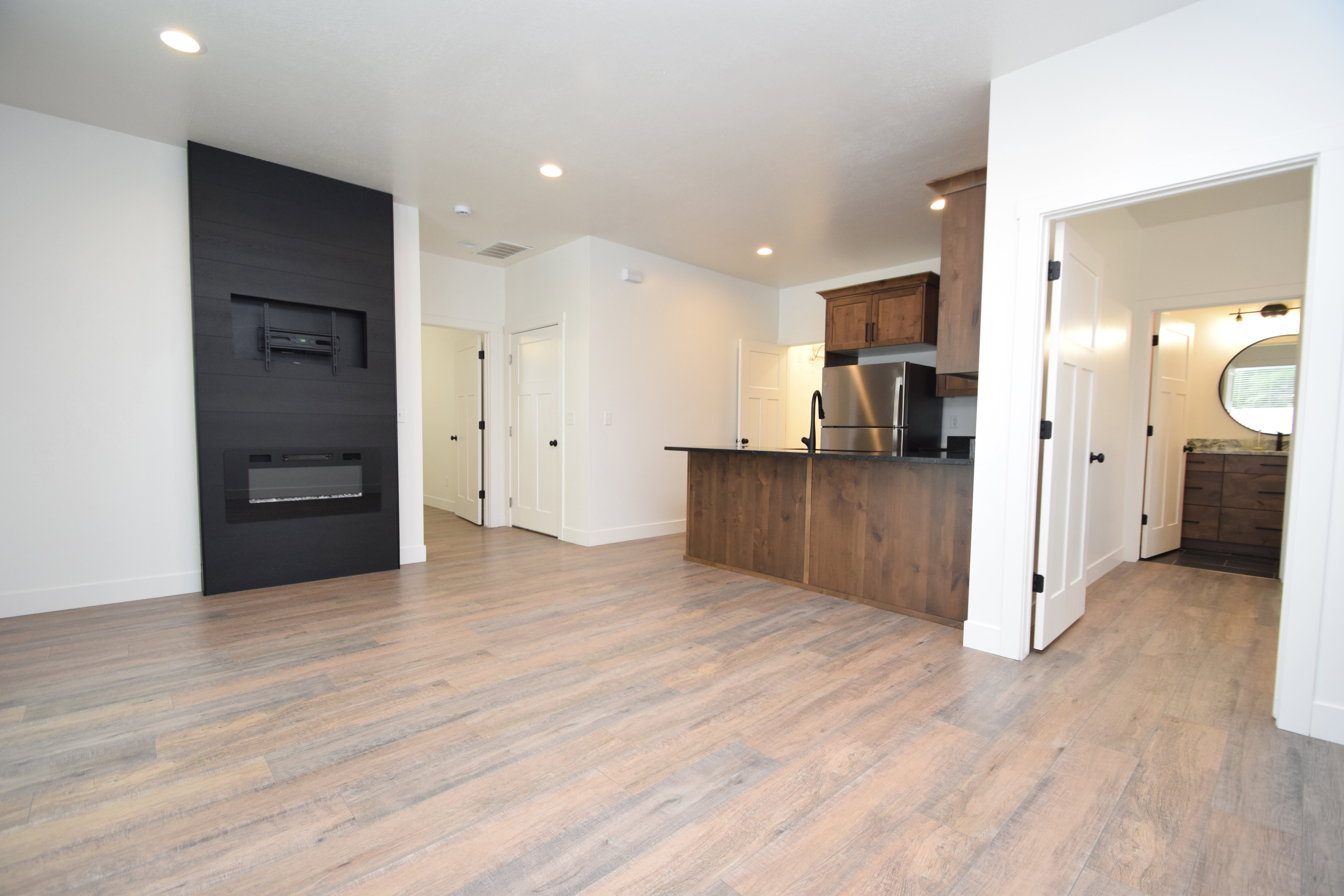 Open-concept living space featuring wood-finish flooring, a contemporary fireplace with a sleek black surround and integrated media niche, recessed lighting, a kitchen island with dark wood-finish cabinetry, and stainless steel appliances