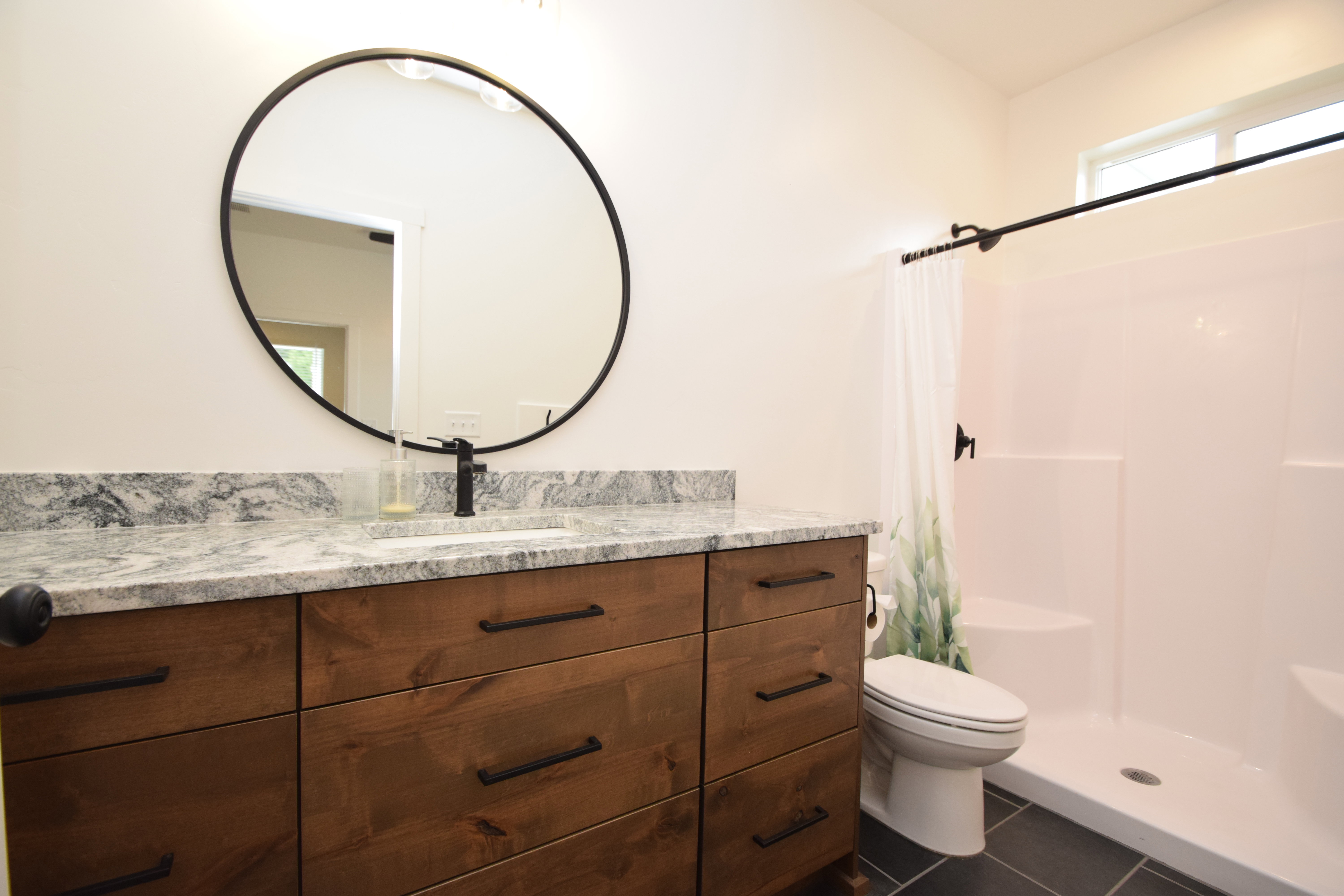Bathroom featuring a wood-finish vanity with drawer storage, a stone-finish countertop, an undermount sink, and a matte black faucet