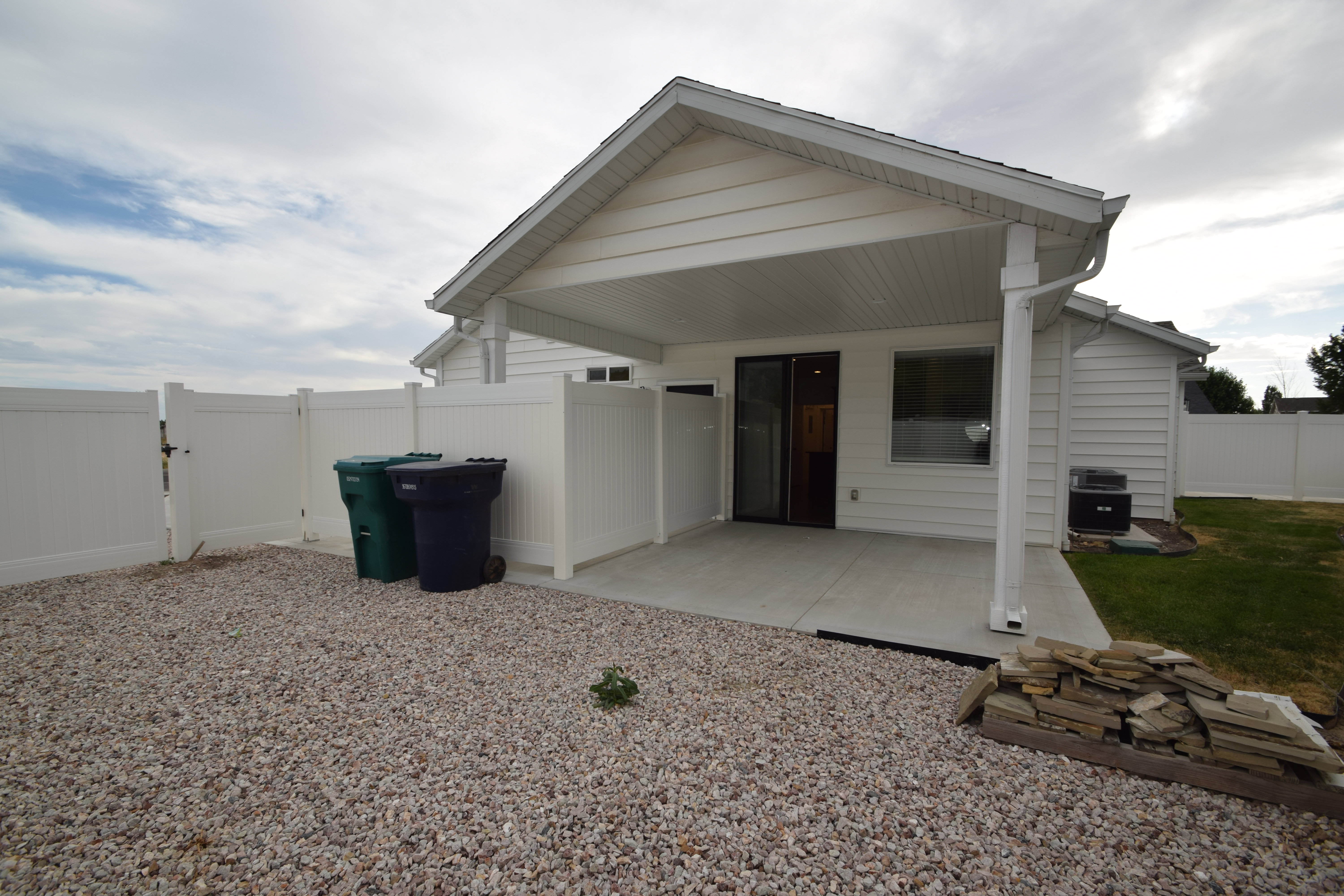 Covered patio with concrete flooring, framed by white vinyl fencing