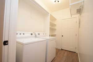 Dedicated laundry area featuring a washer and dryer, built-in shelving, wood-finish flooring, and recessed lighting