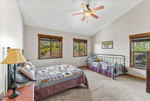 Vaulted ceiling bedroom featuring multiple windows with wood trim, ceiling fan, and carpeted flooring