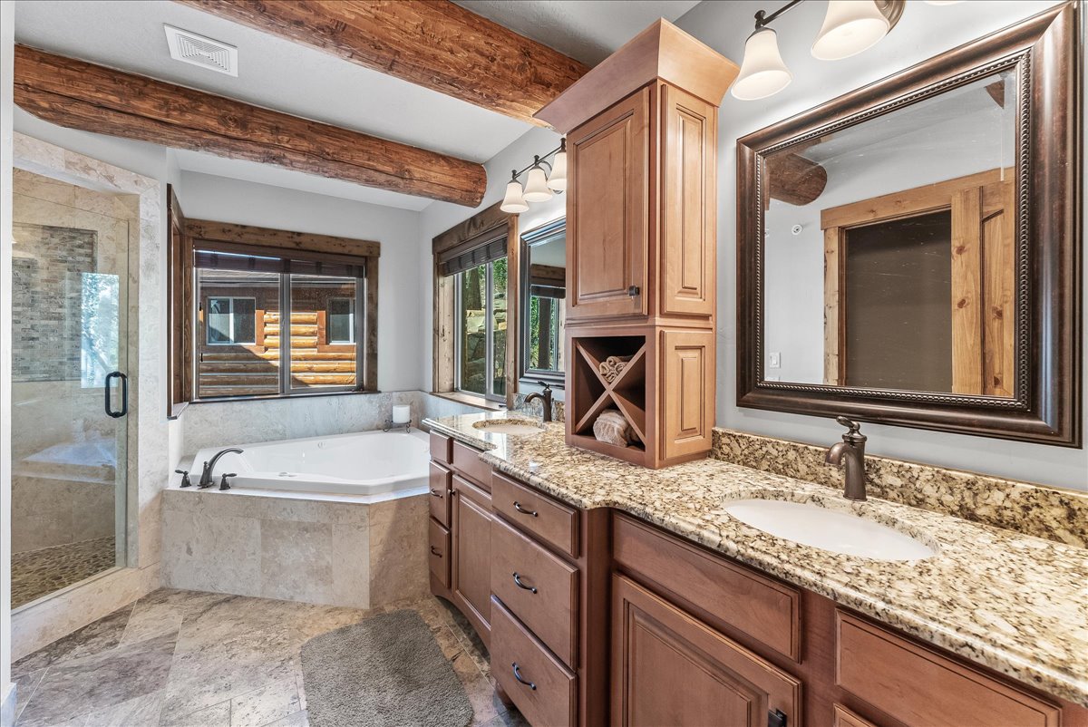 Bathroom featuring exposed wood beams, a corner jetted tub, and a separate glass-enclosed shower with stone tile