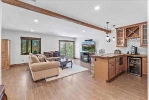 Spacious entertainment area featuring wood-finish flooring, exposed ceiling beam, recessed lighting, and a built-in wet bar with a beverage cooler and wood cabinetry