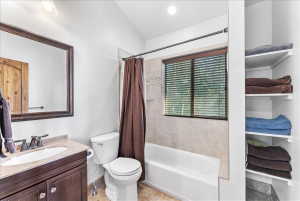 Bathroom featuring a tub/shower combination with tile surround, a built-in window with horizontal blinds, and a dark wood-finish vanity with a light-colored countertop and undermount sink