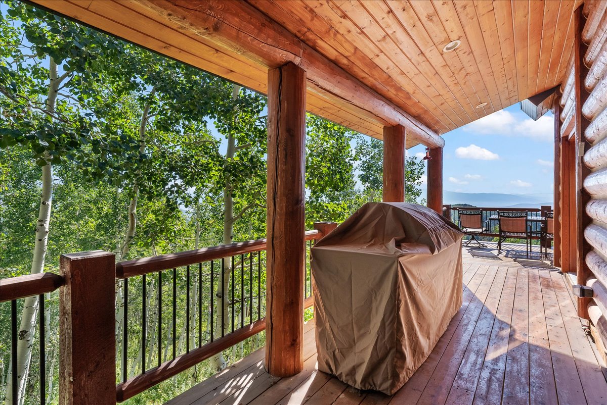 Expansive wood deck featuring a natural wood ceiling, log support beams, wood railing with black spindles, and mountain scenery