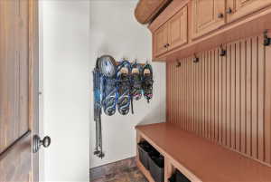 Built-in mudroom storage featuring a wood bench, slatted wood paneling with hooks, and upper cabinetry