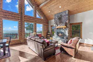Expansive great room featuring a floor-to-ceiling stone fireplace with a wood mantel, exposed log walls, and wood-finish flooring