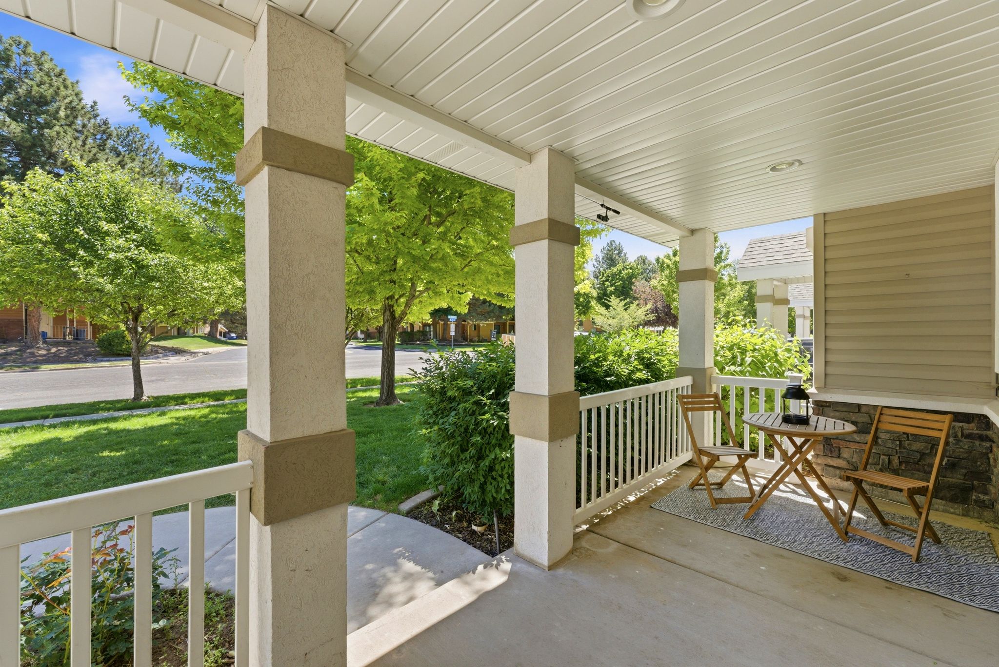 Covered front porch featuring textured columns with accent bands, a white railing, a concrete floor, and recessed lighting