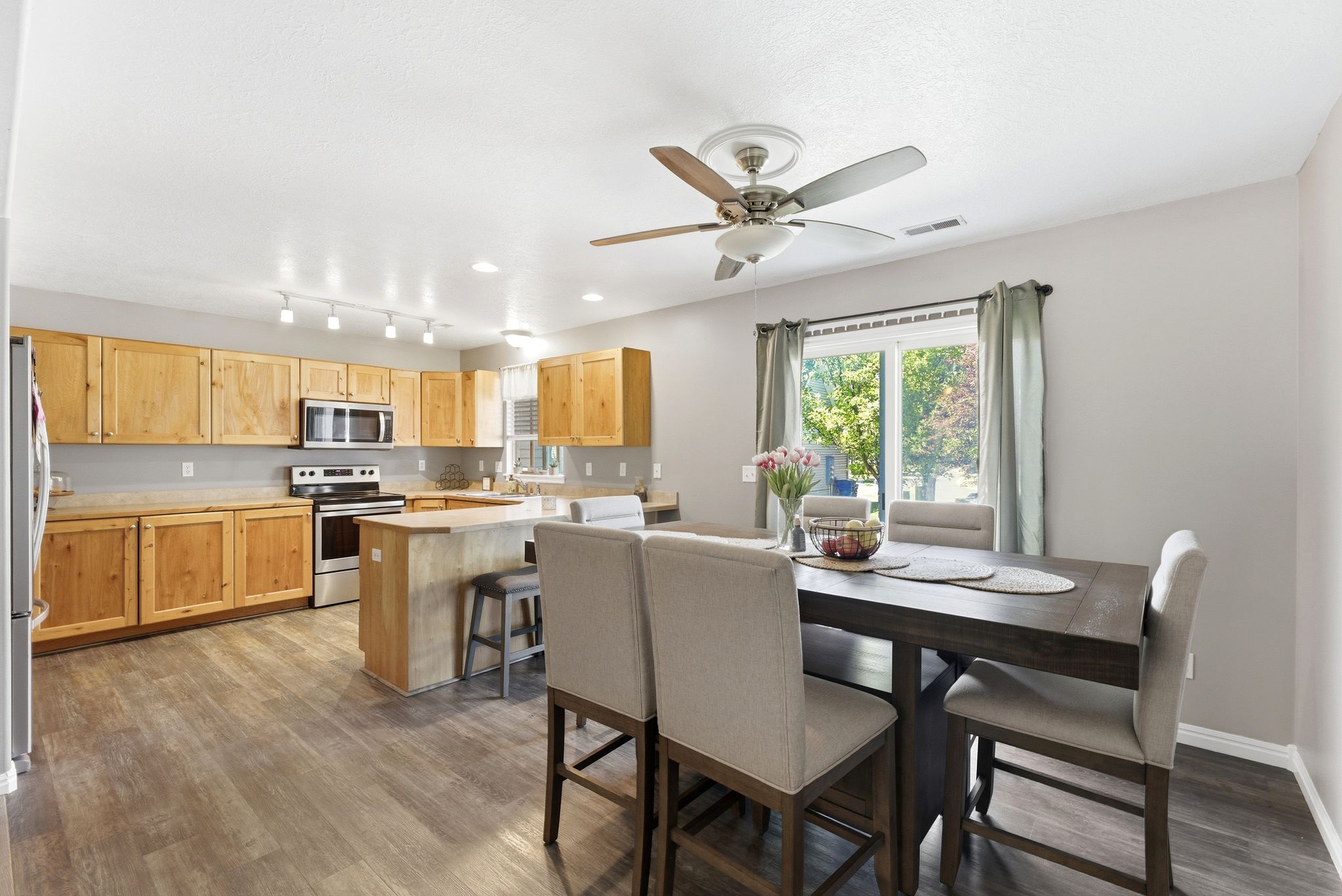 Open-concept kitchen and dining area featuring wood-finish flooring, light wood cabinetry, stainless steel appliances, a kitchen island with seating, and a sliding glass door