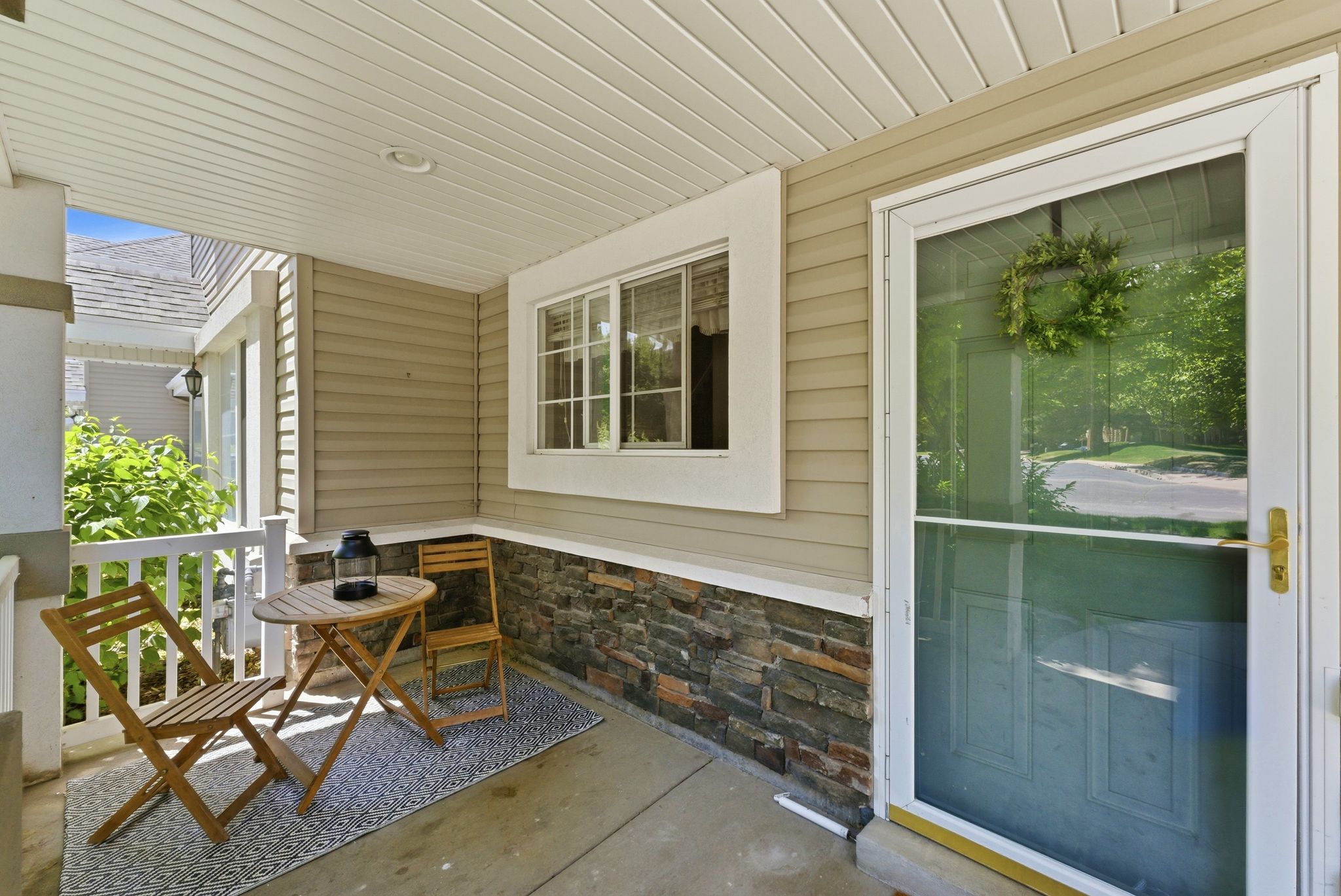 Covered front porch featuring a stone accent wall, vinyl siding, a multi-pane window, and a white storm door