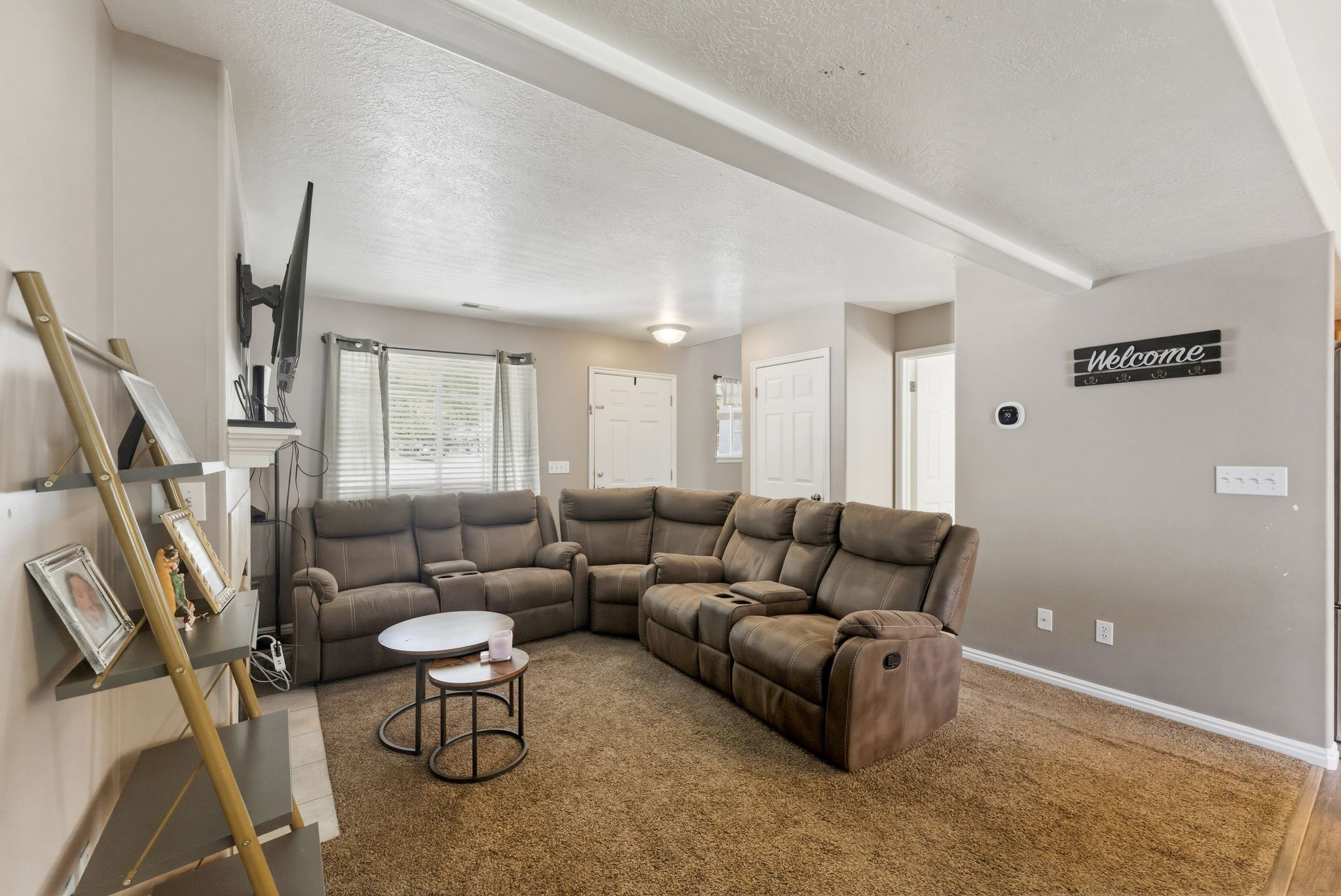 Carpeted living area featuring a neutral color palette, white baseboards, and ceiling beams