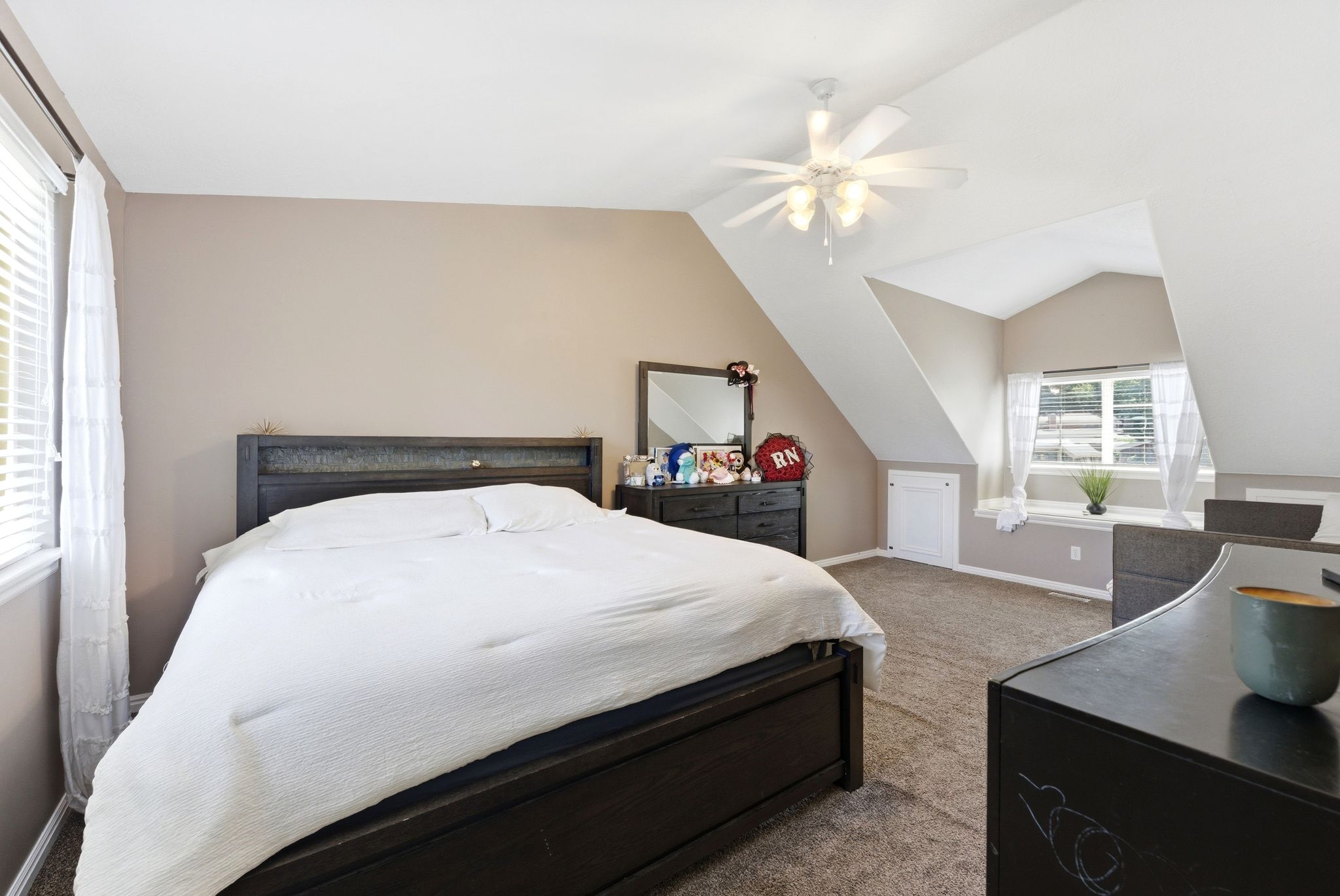Bedroom featuring sloped ceilings, recessed window with blinds, light tan wall paint, and gray carpet flooring