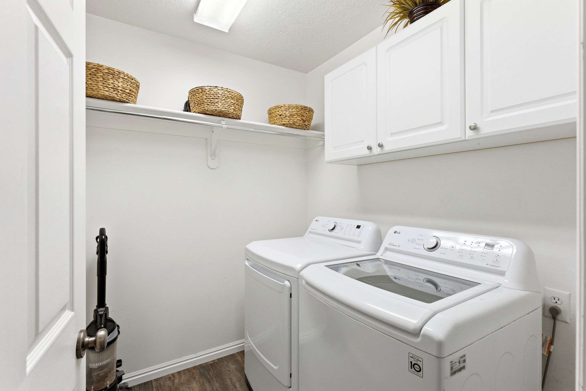 Dedicated laundry space featuring white cabinetry with brushed nickel hardware, a white upper shelf, and wood-finish flooring