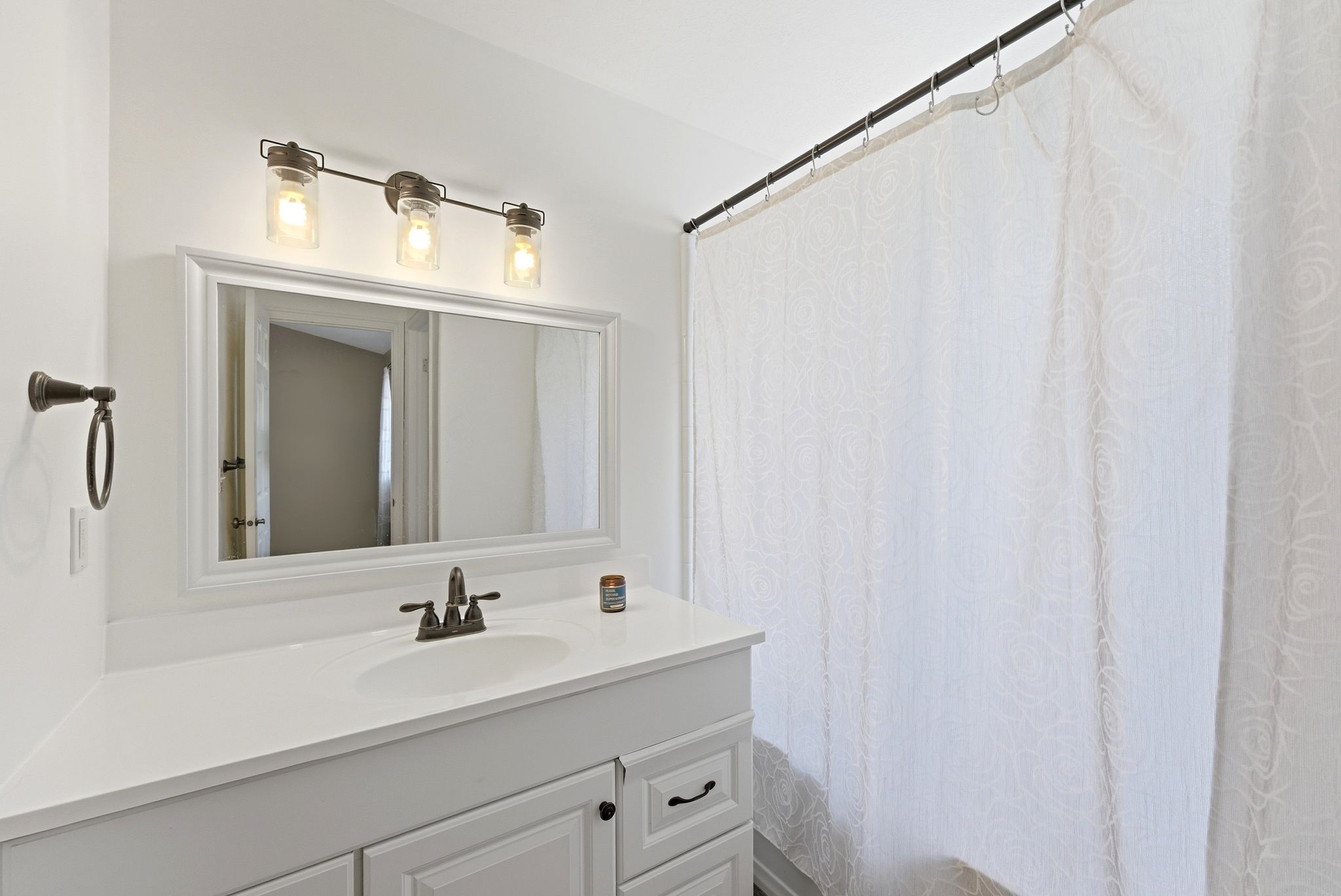 Bathroom vanity with a rectangular undermount sink, bronze-finish faucet, and white countertop