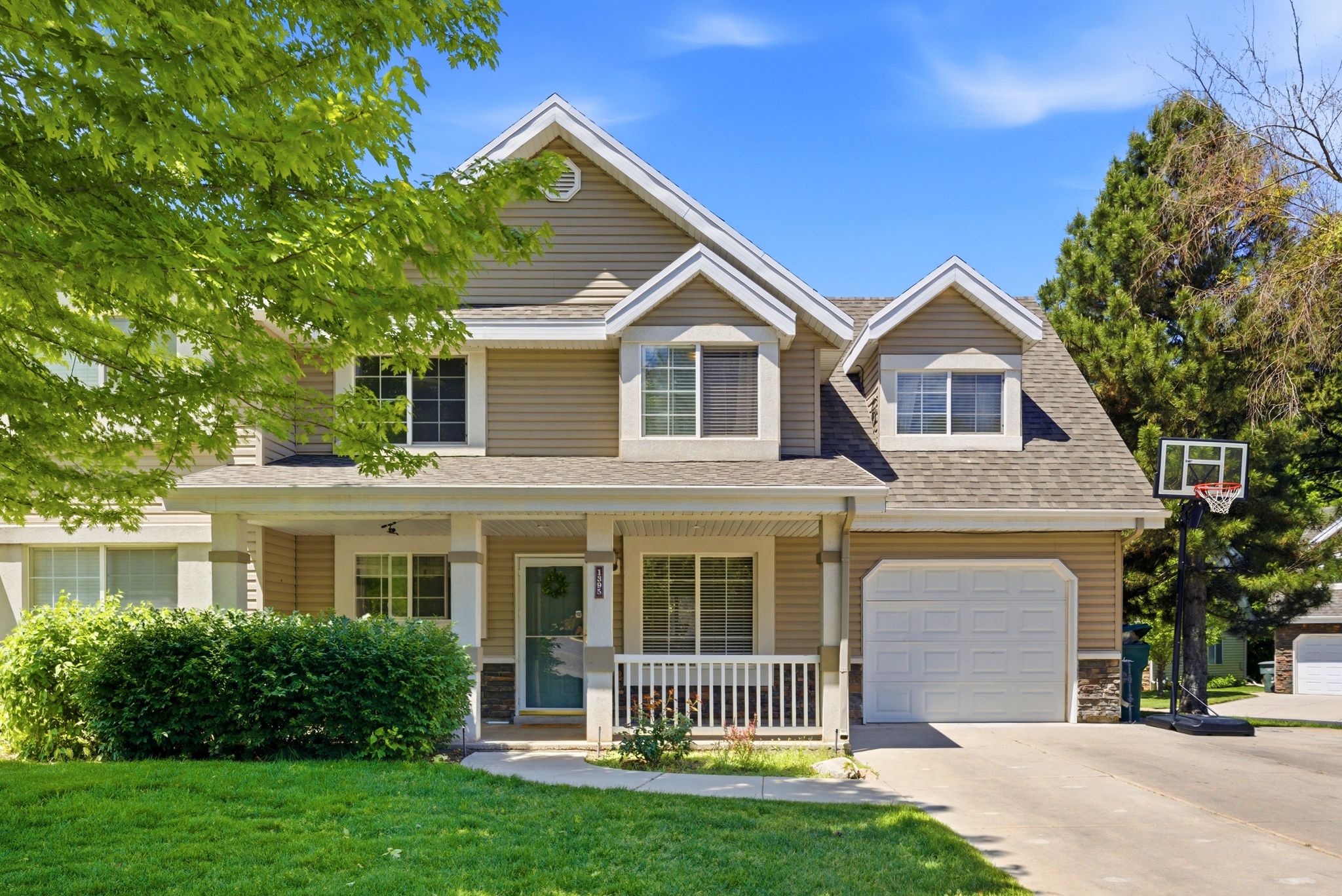 Multi-level residence featuring a covered front porch with white railings, a two-car garage, and dormer windows