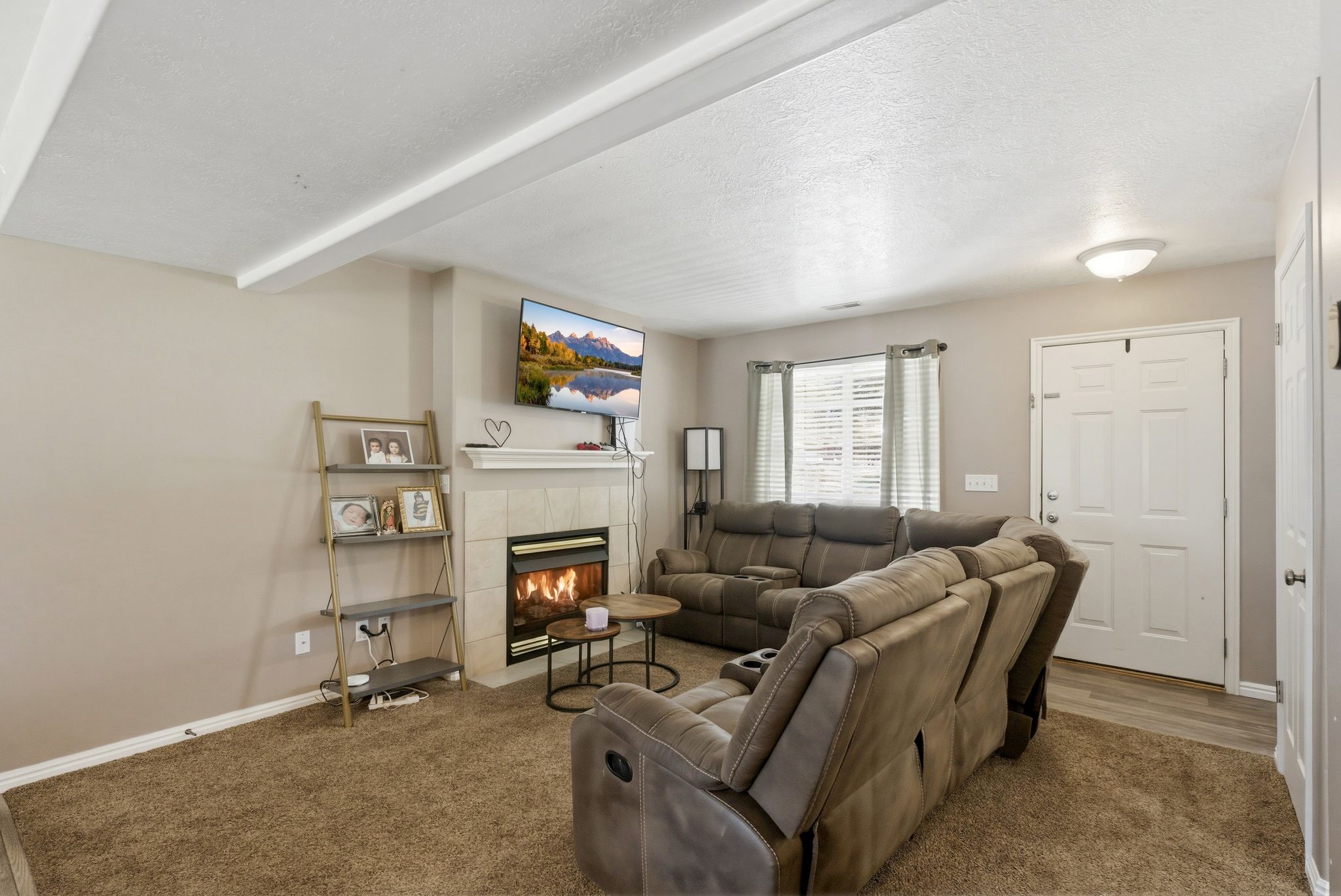 Living area featuring a fireplace with a tile surround and mantel, wood-finish flooring at the entry, and a ceiling with exposed beams