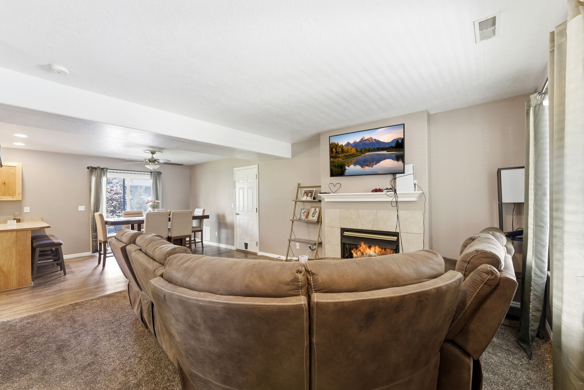Living area featuring a fireplace with a stone surround and mantel, wood-finish flooring, and a dining area with a ceiling fan