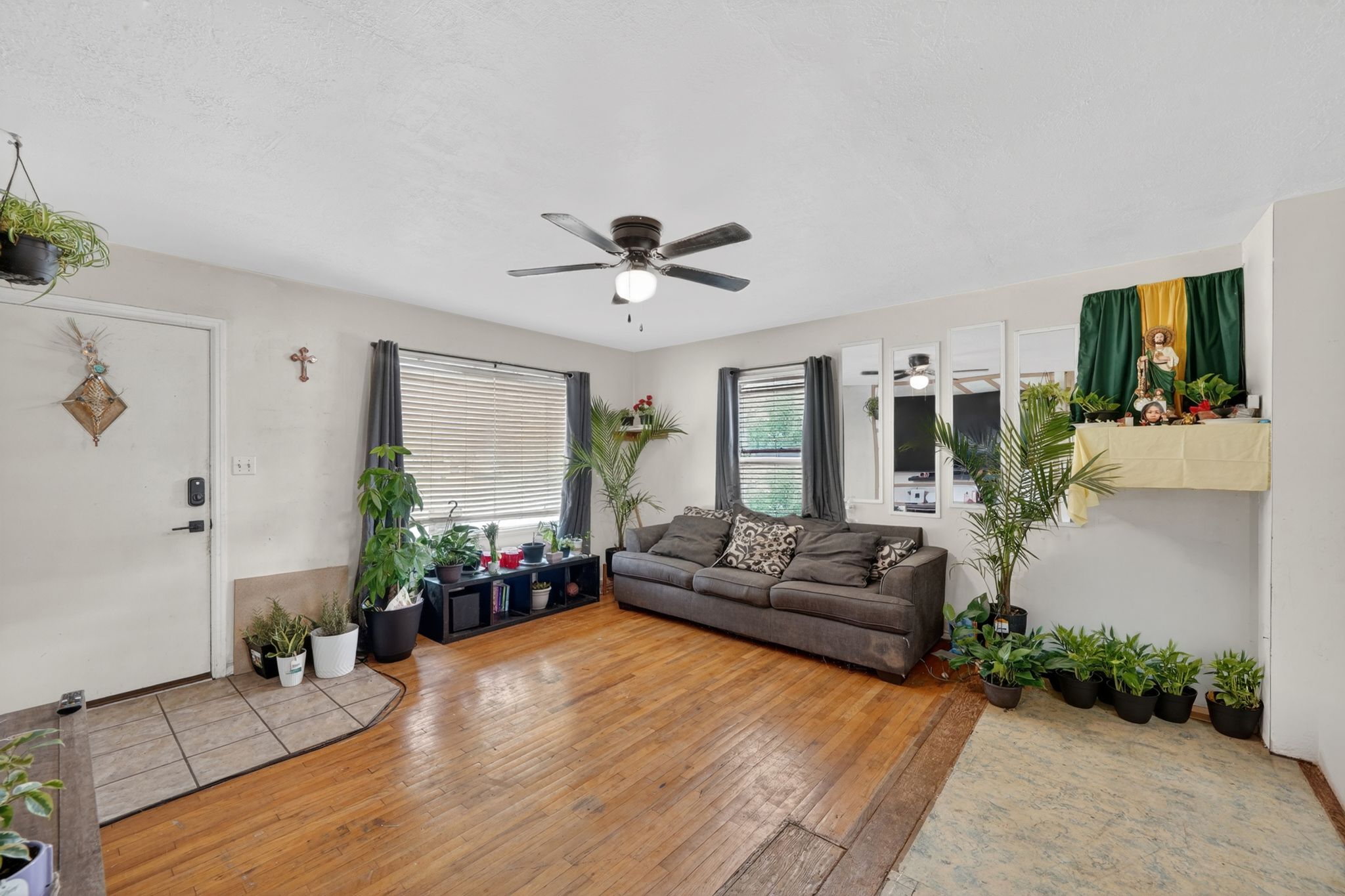 Living area featuring wood-finish flooring, a ceiling fan with integrated lighting, and multiple windows with horizontal blinds