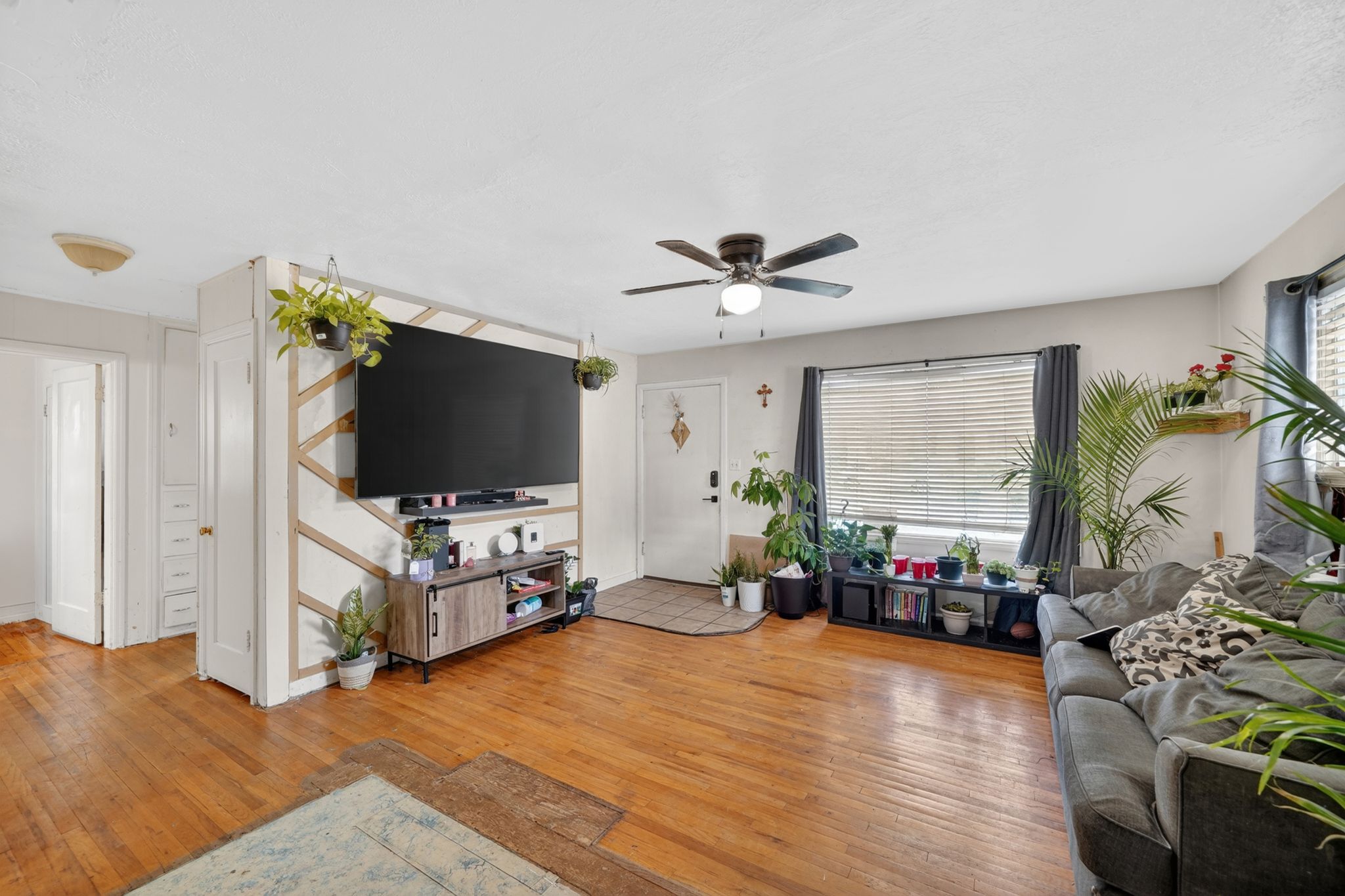 Bright living area featuring wood-finish flooring, a ceiling fan with integrated lighting, and a large window with blinds