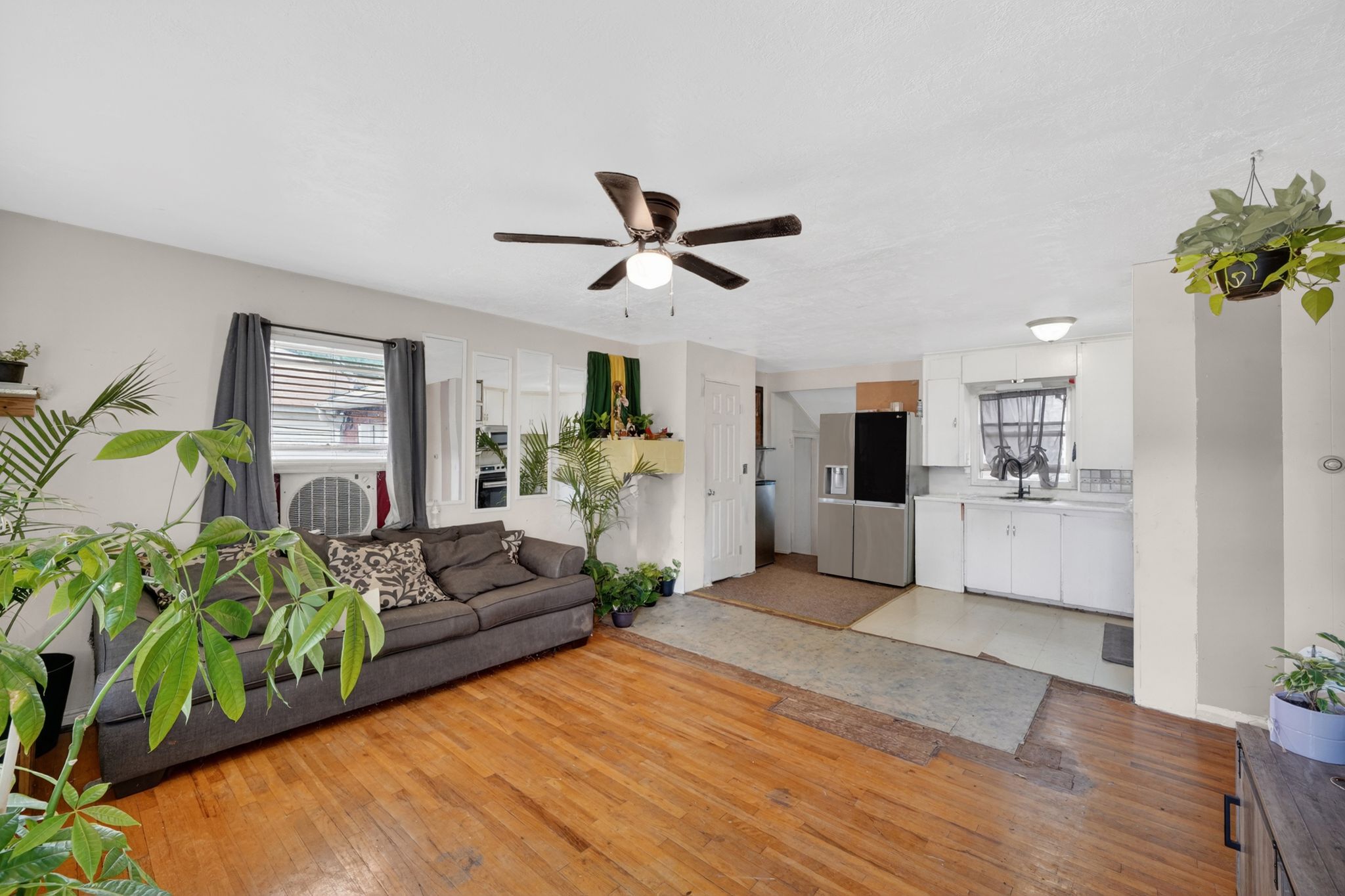 Spacious open-concept living area featuring wood-finish flooring, a ceiling fan with integrated lighting, and a window with blinds