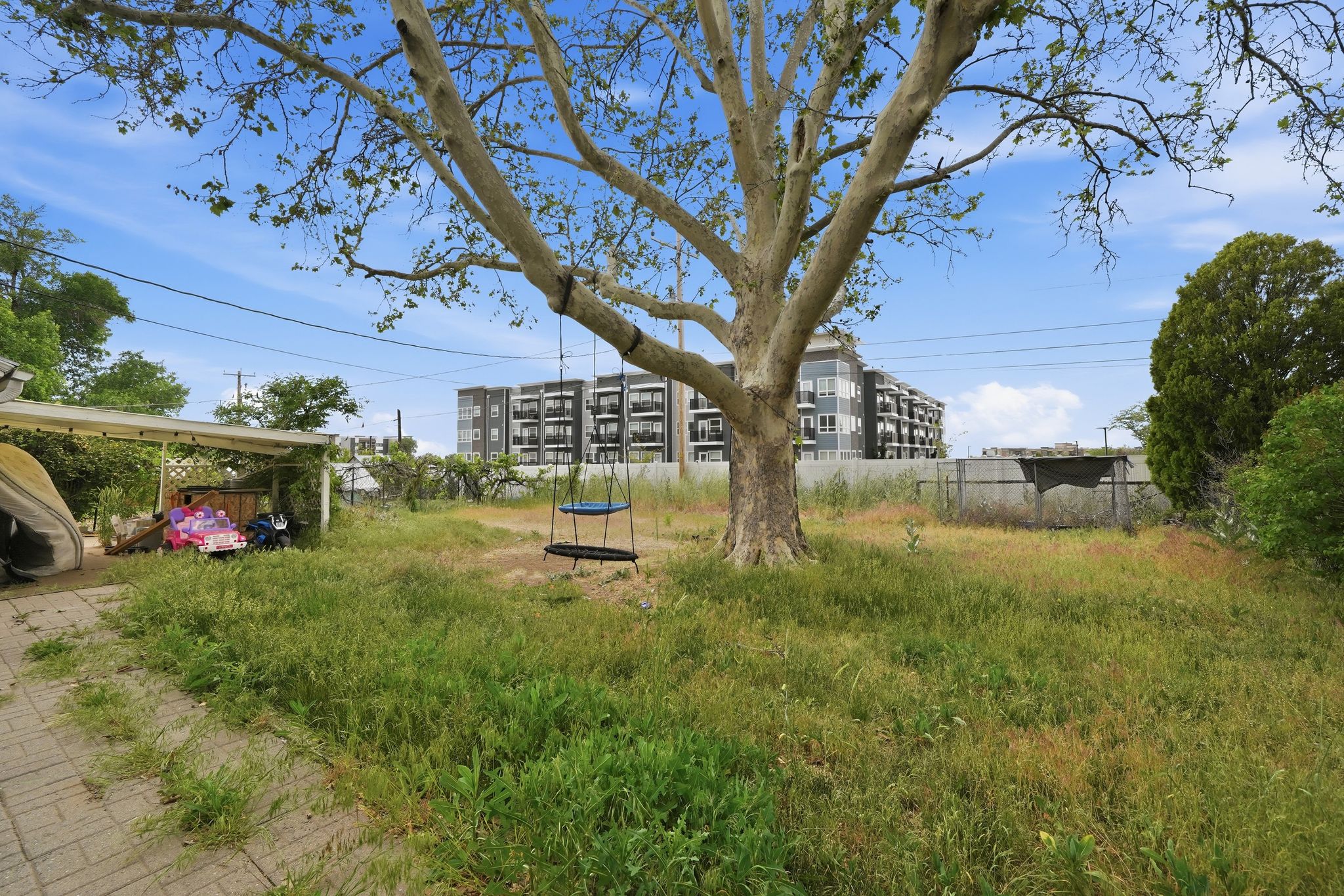 Expansive outdoor space featuring a large mature tree, established perimeter fencing, and a paved patio area