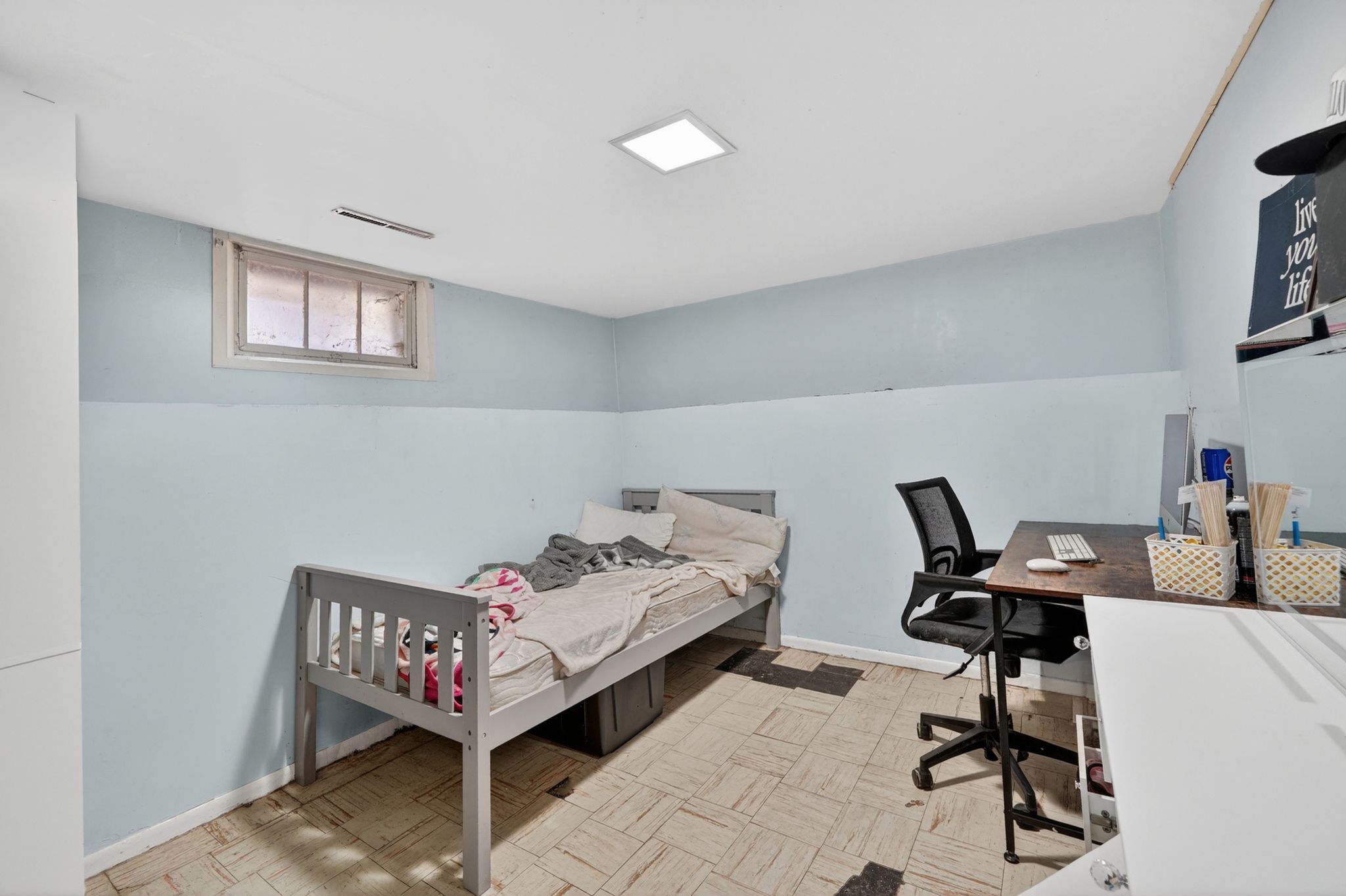 Recessed square lighting illuminates this room, featuring a high window with white trim, light blue wall paint, and patterned floor tiling