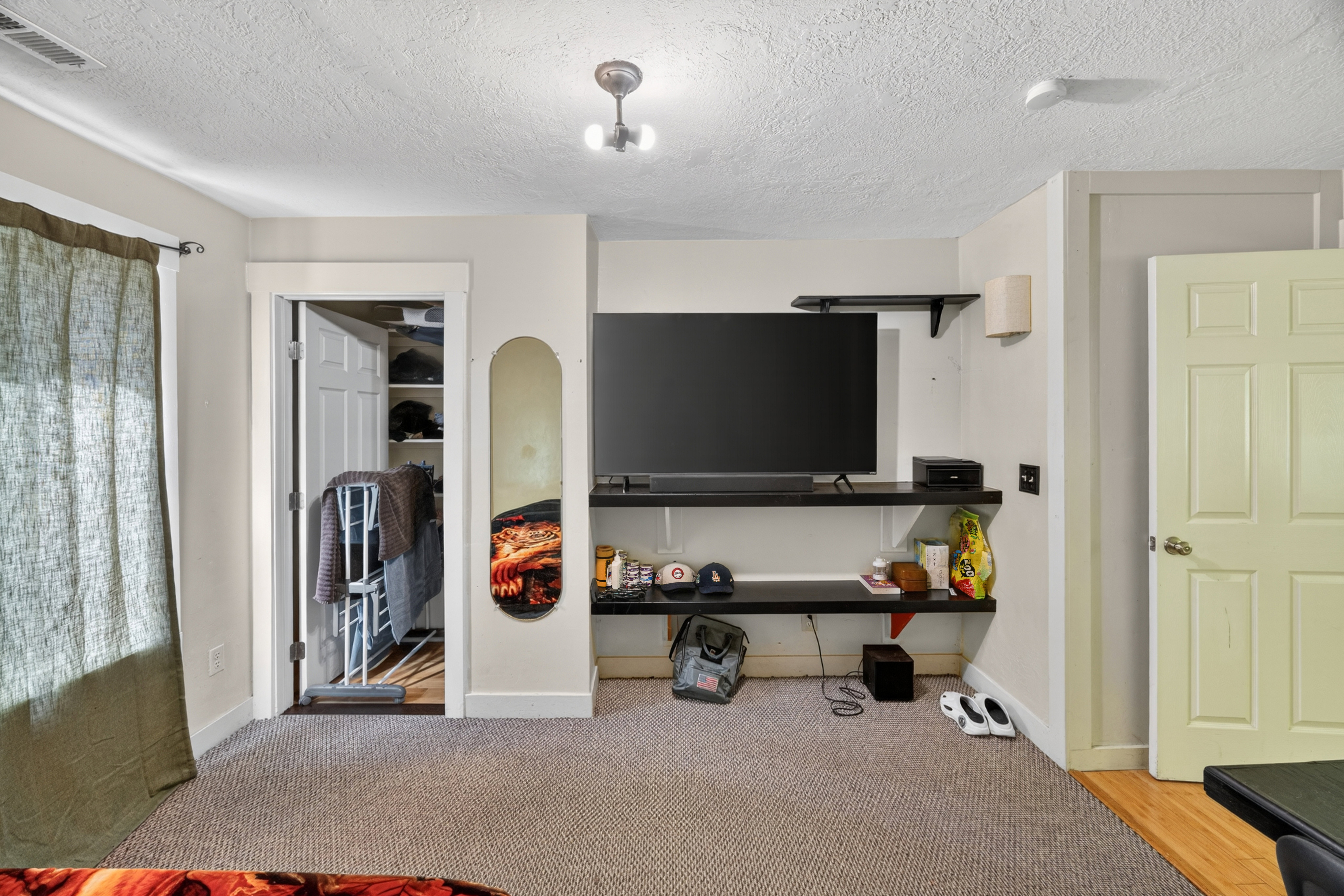 Carpeted room featuring a built-in closet with shelving, a window with curtain rod, a ceiling light fixture, and a paneled door