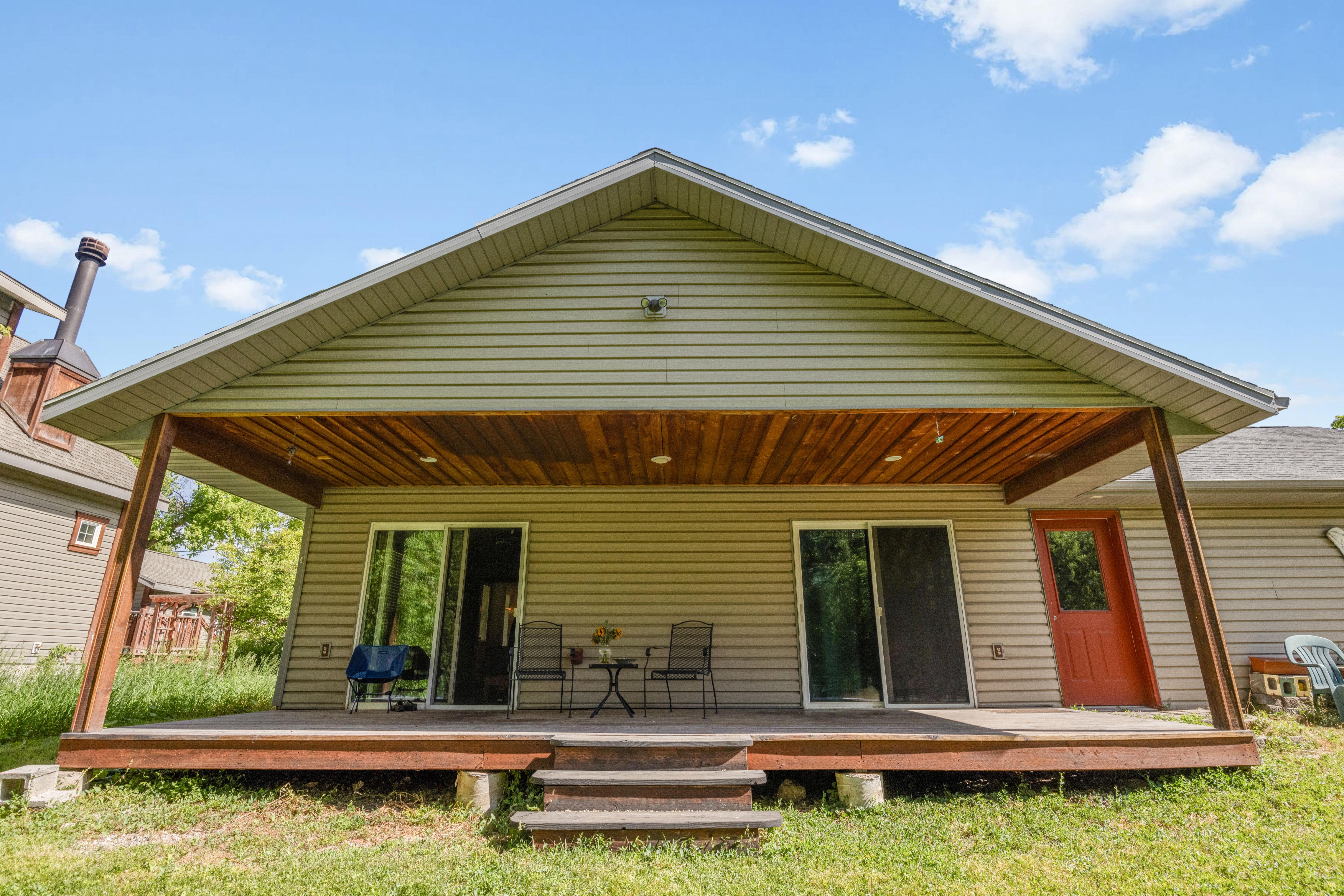 Rear exterior featuring a covered deck with a wood-finish ceiling, two sliding glass doors, a red paneled door, and siding