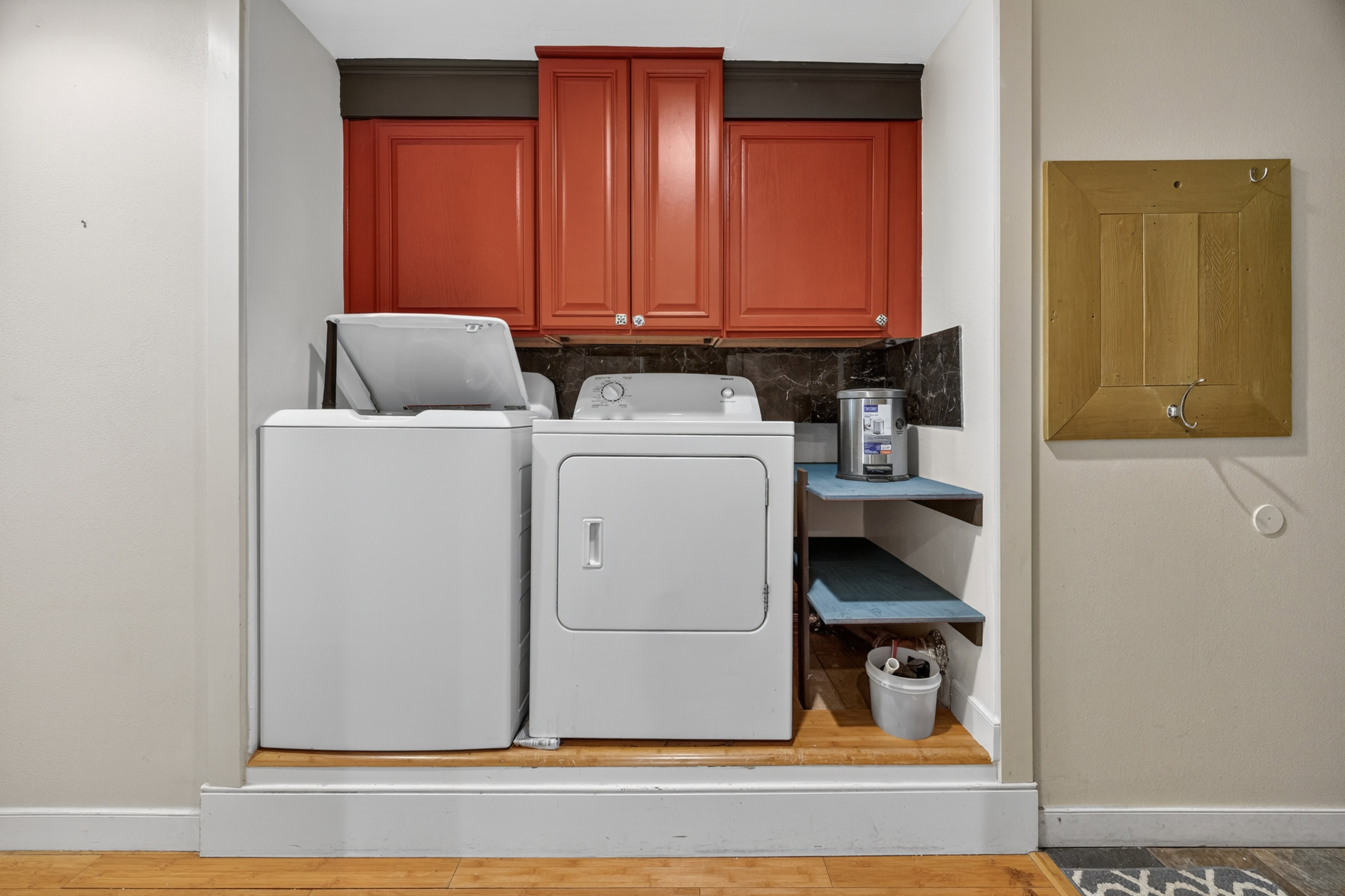 Dedicated laundry area featuring red upper cabinetry, dark stone-finish backsplash, and wood-finish flooring