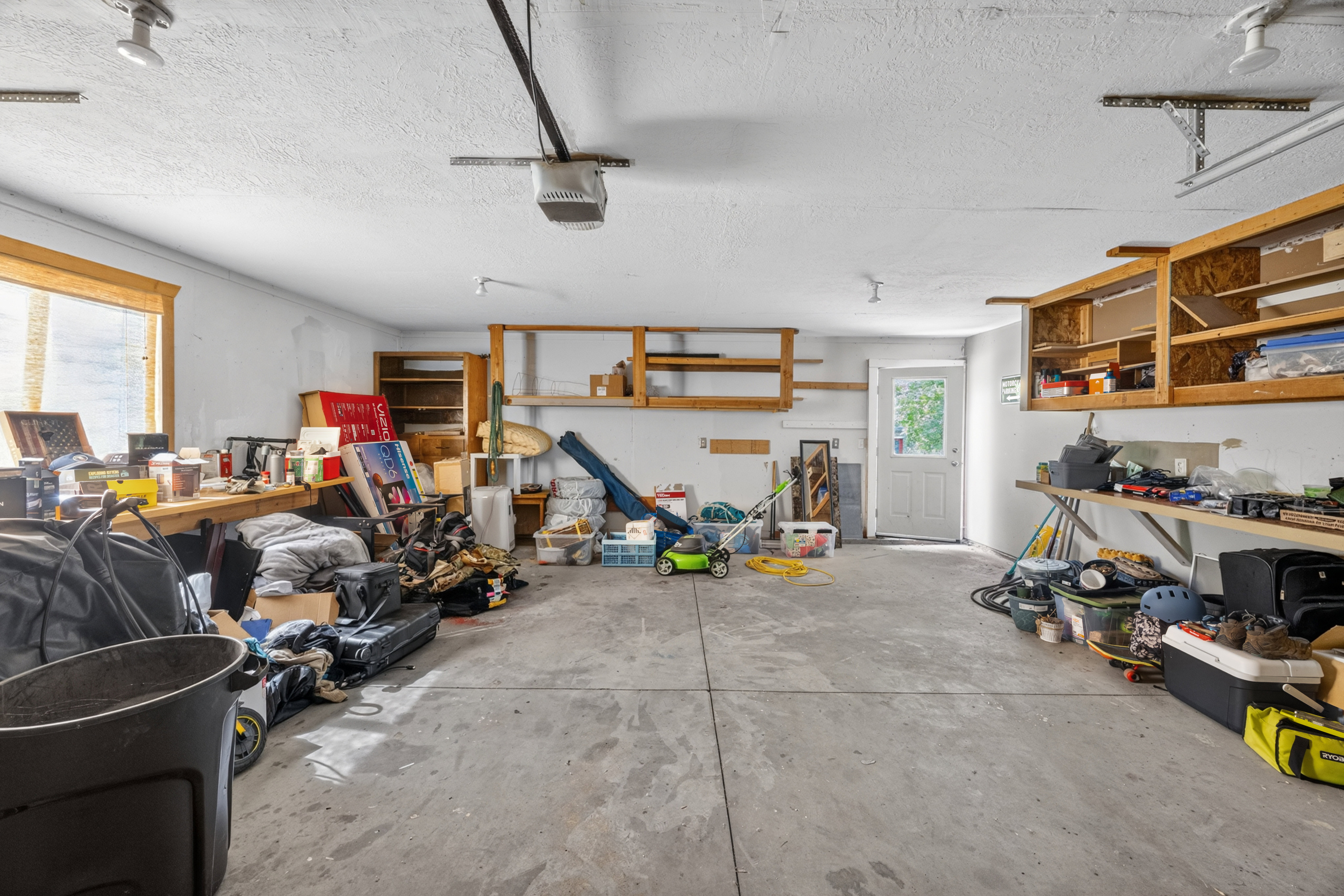 Spacious garage with concrete flooring, multiple built-in shelving units, and a large window providing natural light