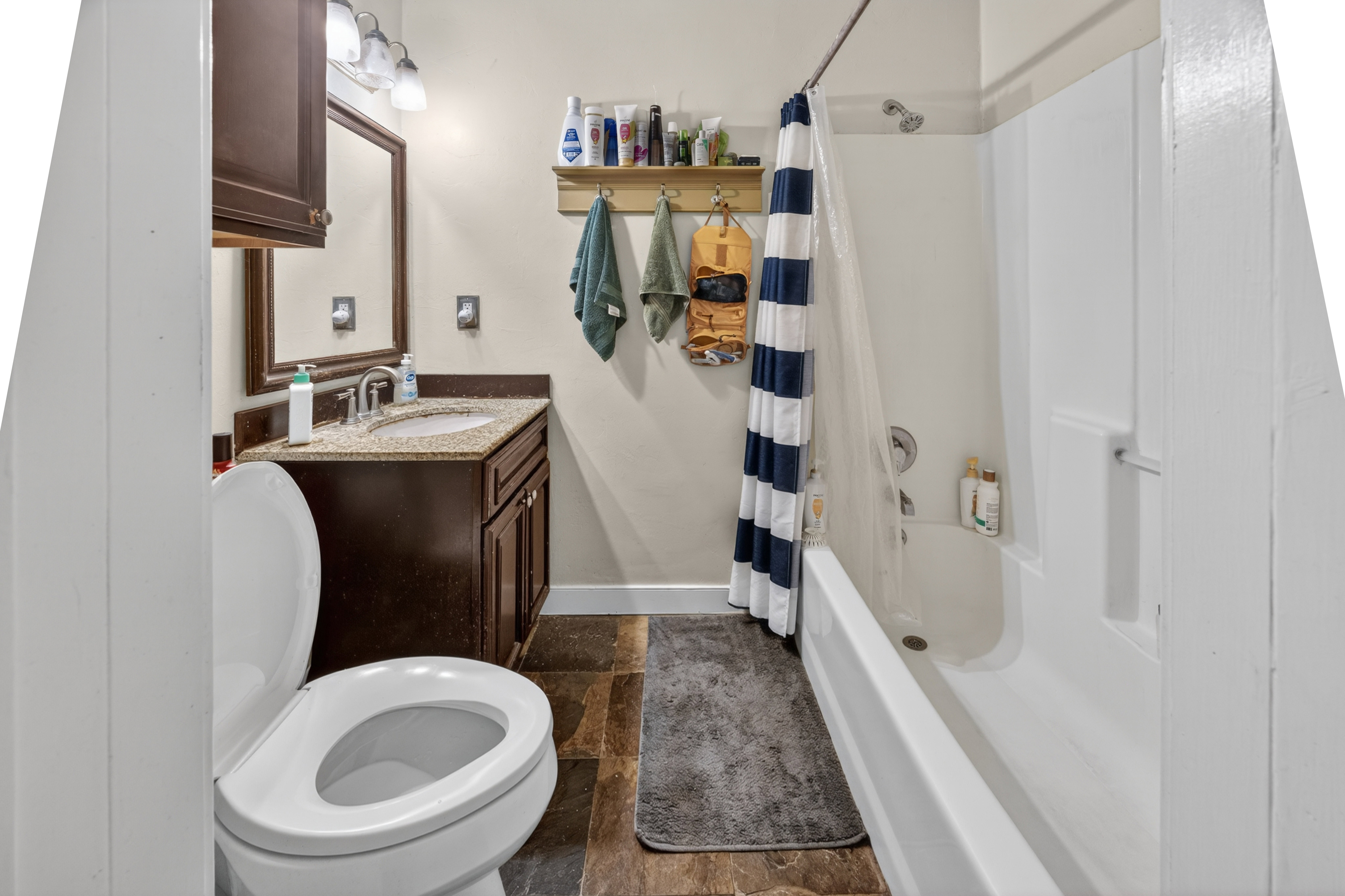 Bathroom featuring wood-finish flooring, a white toilet, a dark wood-finish vanity with a light-colored countertop, and a built-in shower/tub combination