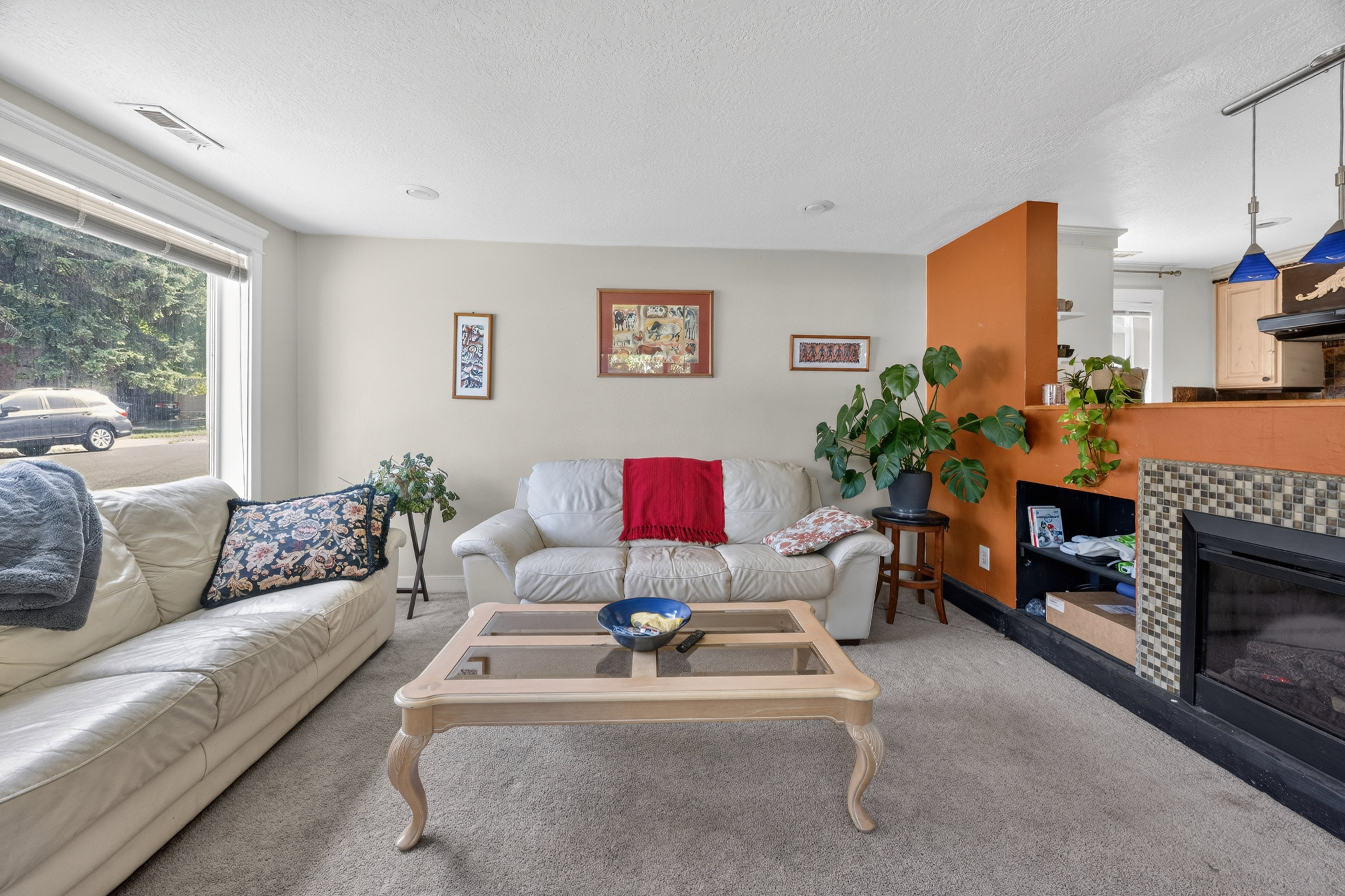 Living area featuring a fireplace with a mosaic tile surround and built-in shelving, large window, recessed lighting, and a partial wall with an orange accent finish