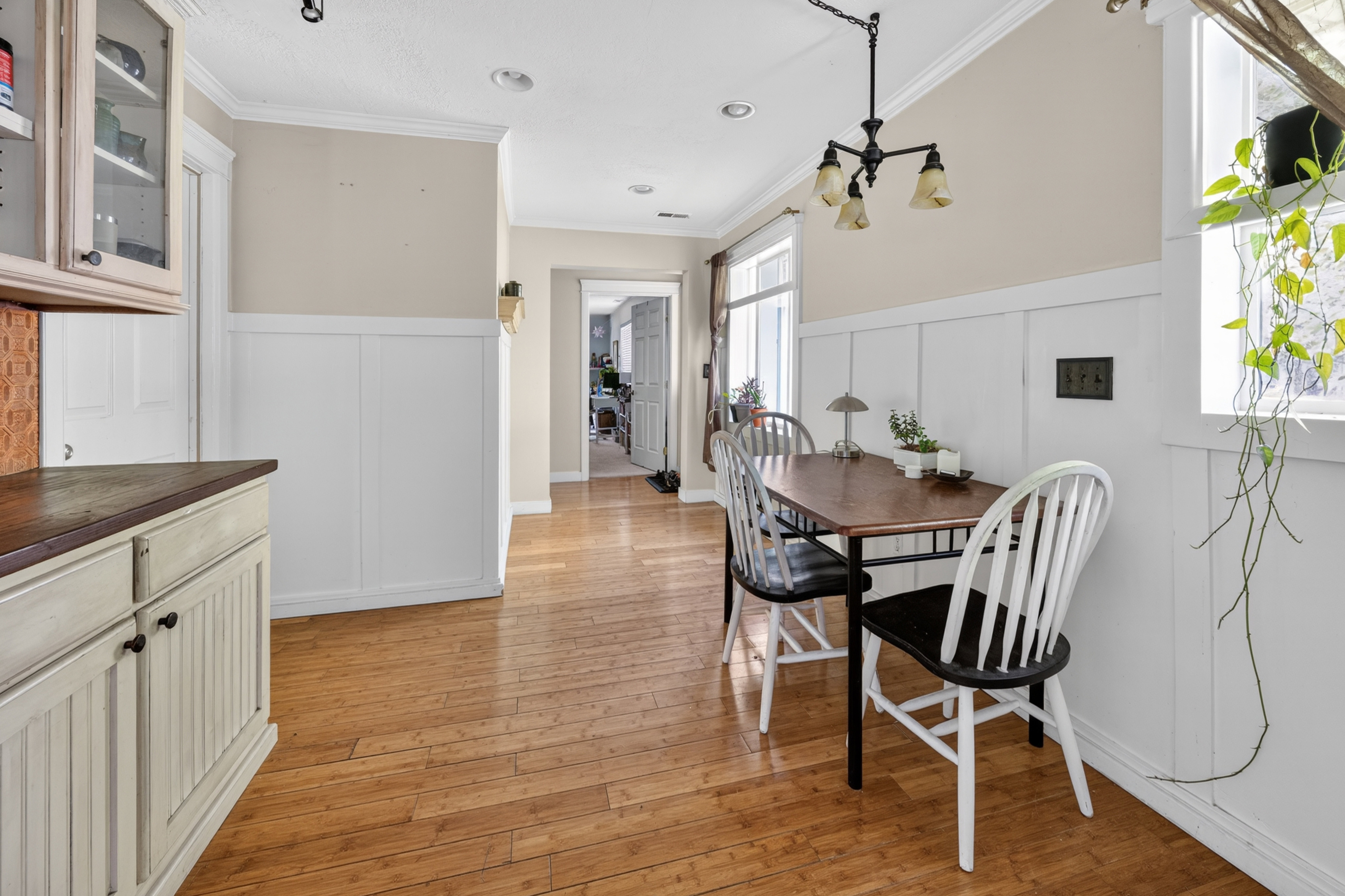 Open-concept dining area featuring wood-finish flooring, white board and batten wainscoting, and crown molding