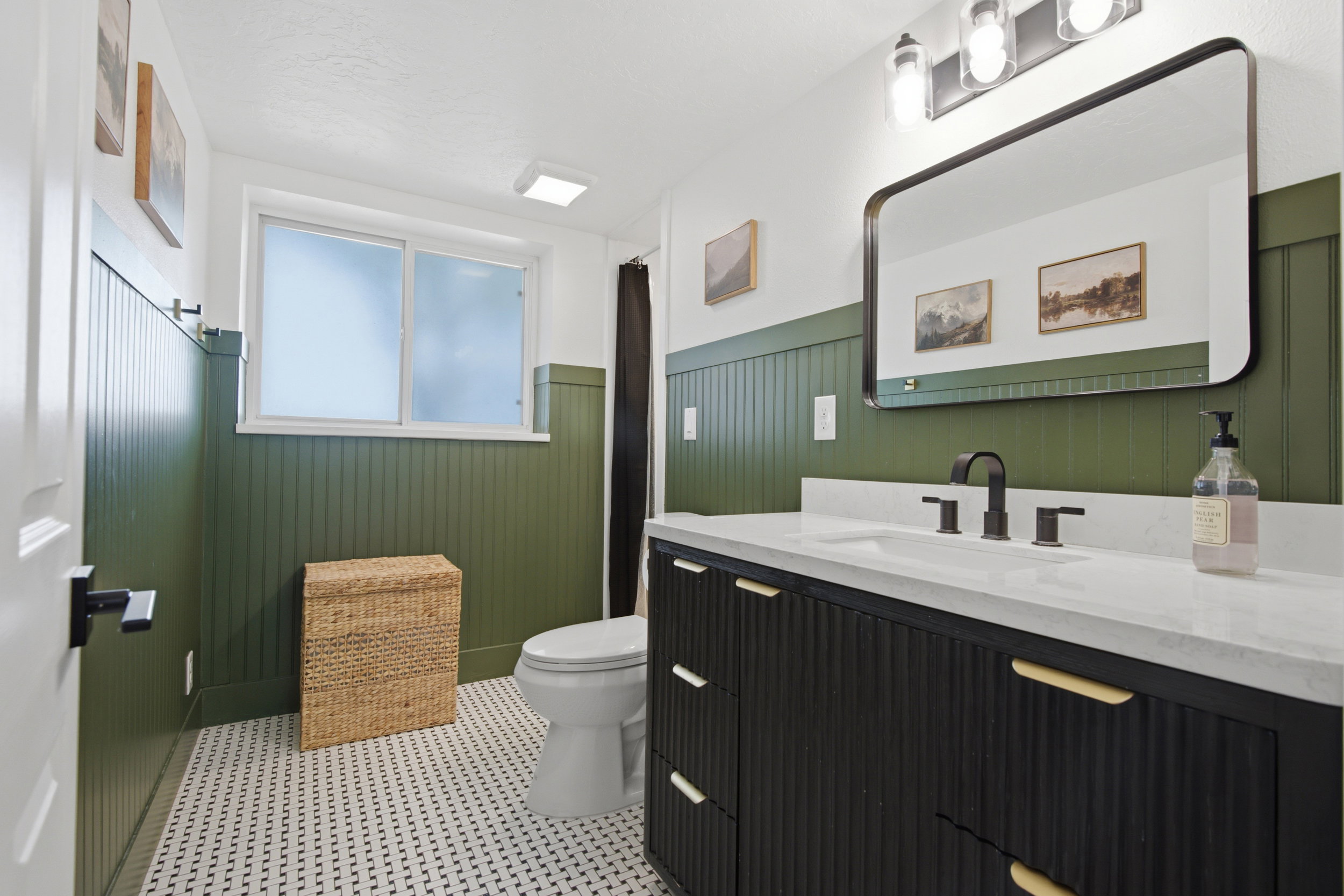 Contemporary bathroom featuring a black fluted vanity with a white countertop and matte black hardware, a rectangular framed mirror, and a three-light fixture