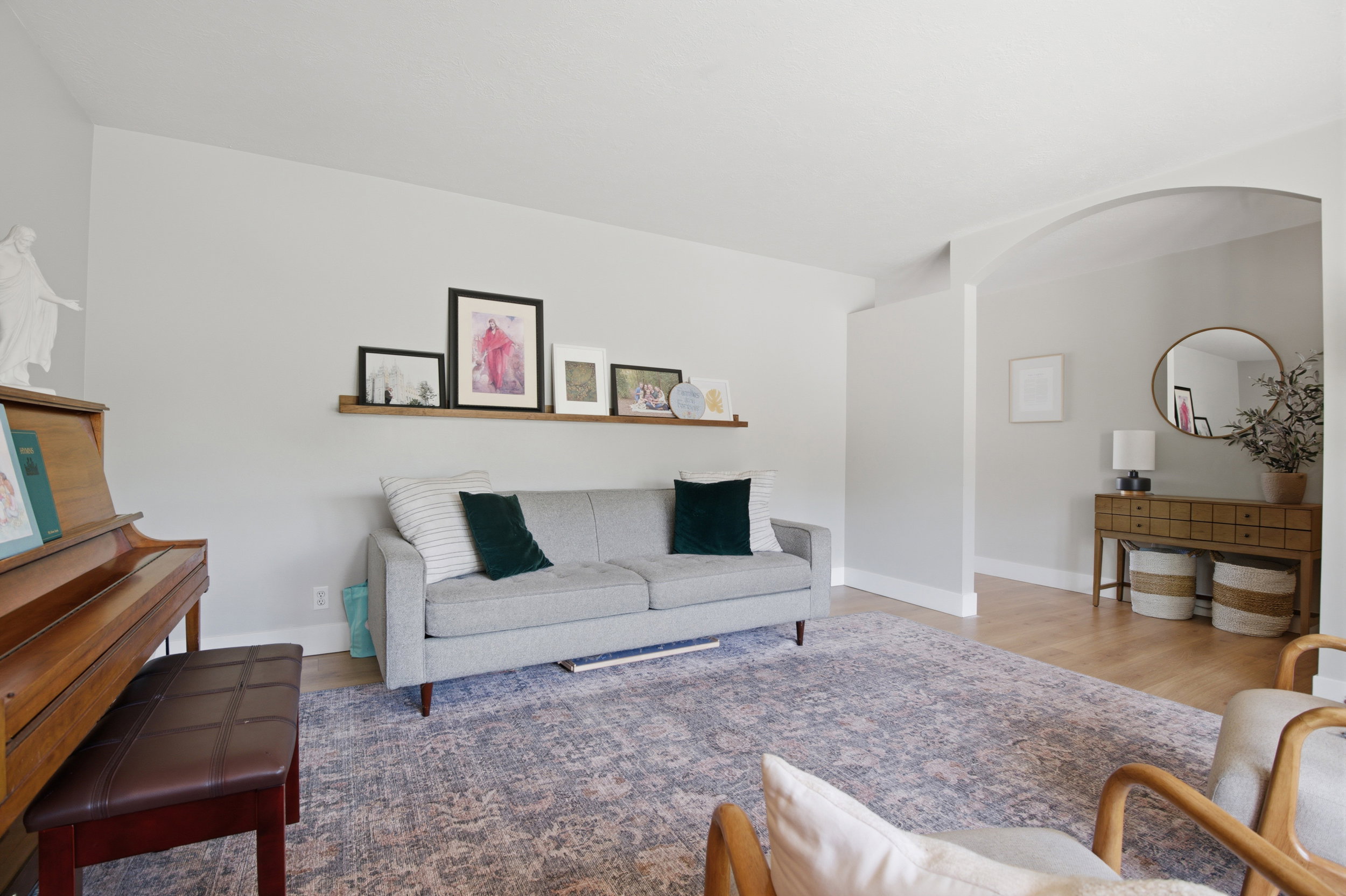 Spacious living area featuring light-toned walls, wood-finish flooring, and a decorative wall shelf