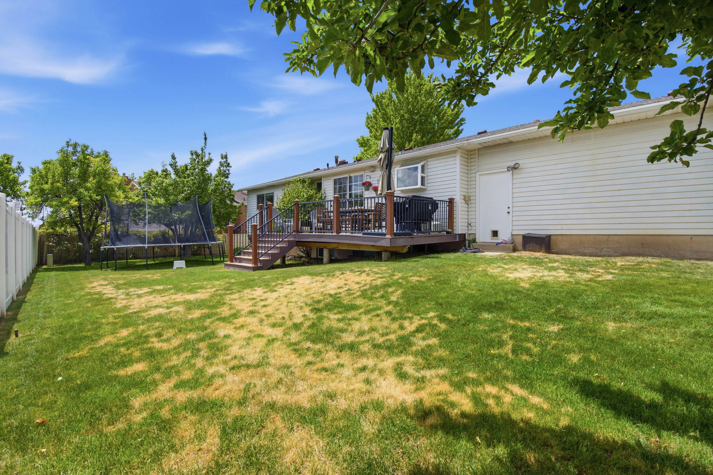 Expansive backyard featuring a multi-level wood deck, white vinyl privacy fencing, and mature trees