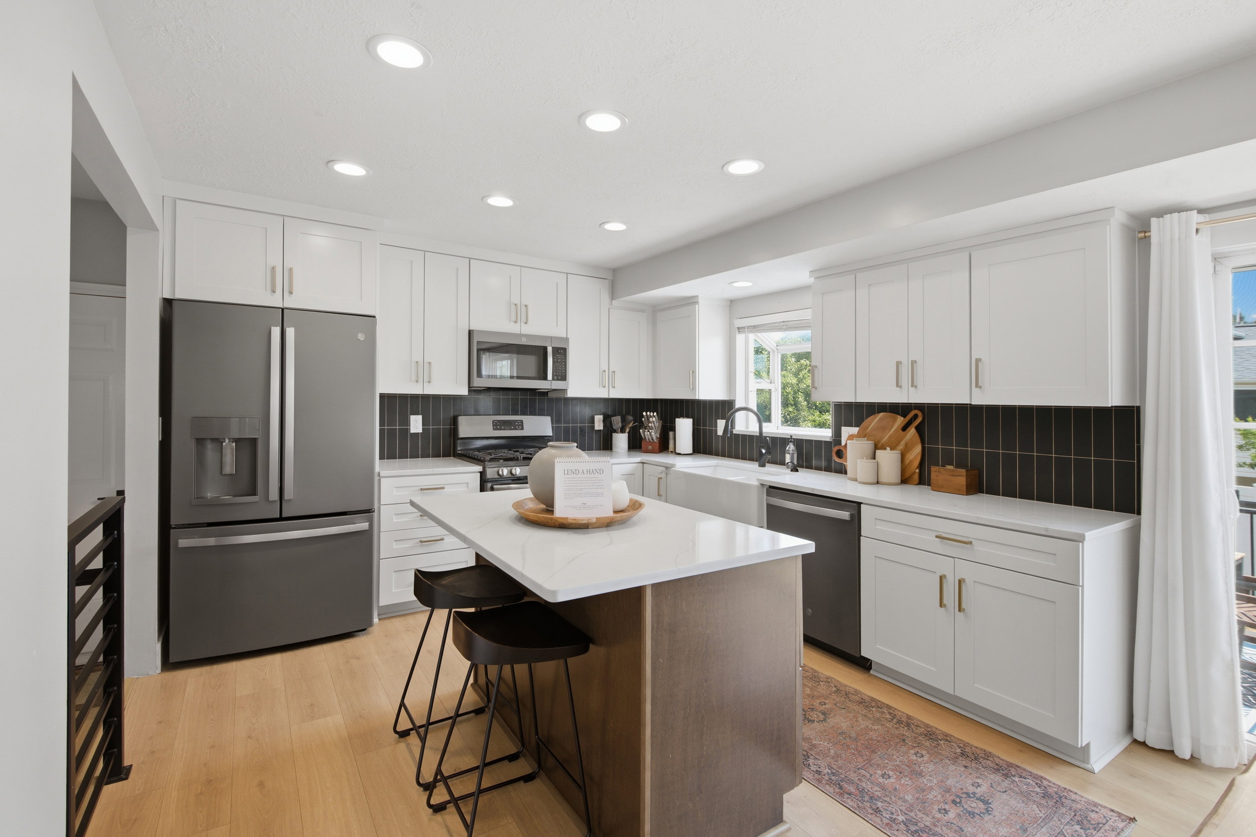 Modern kitchen featuring an island with seating, stainless steel appliances, white cabinetry, black tile backsplash, and light wood-finish flooring