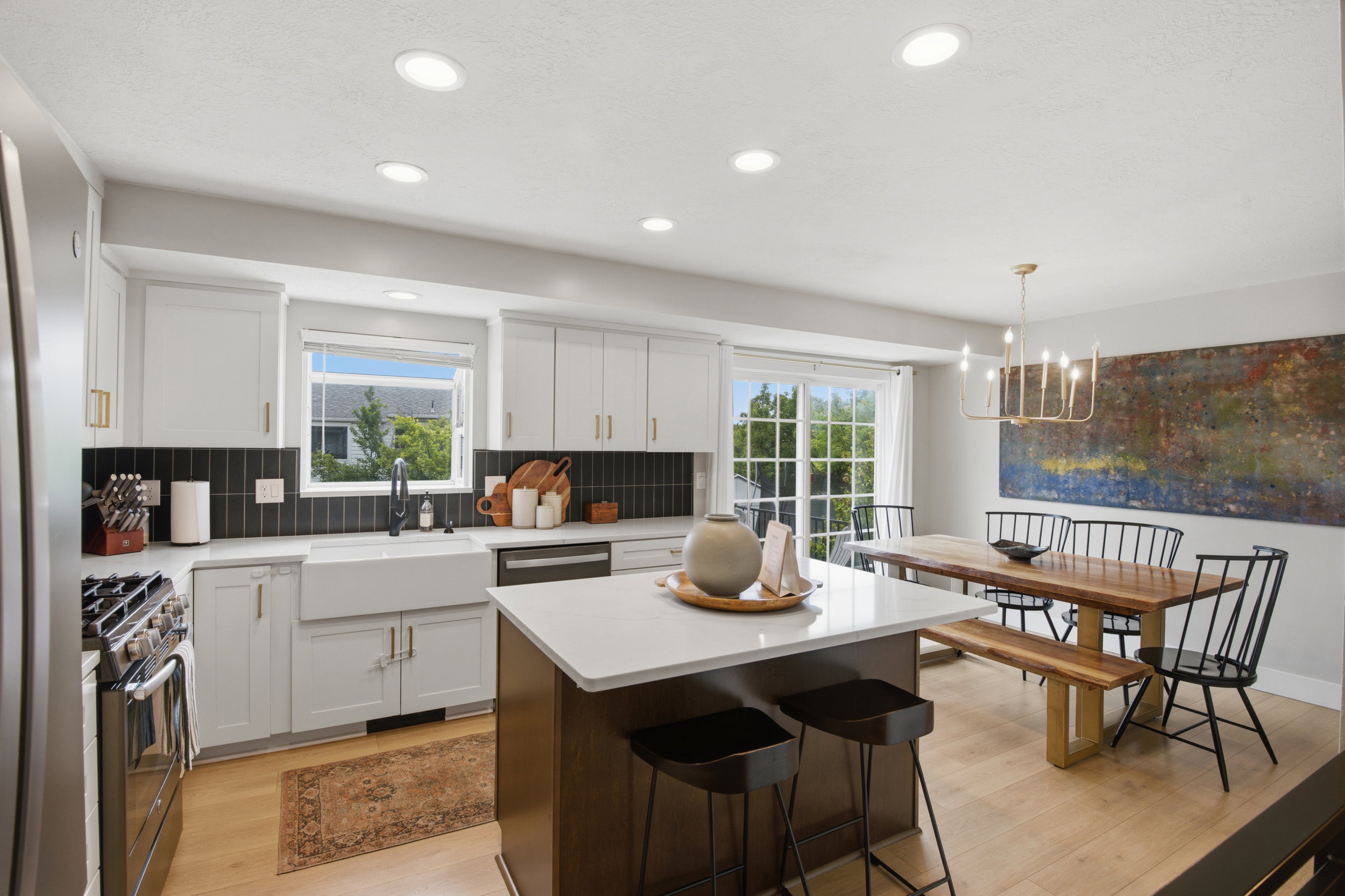 Kitchen featuring white cabinetry, a large farmhouse sink, stainless steel appliances, a center island with countertop seating, and wood-finish flooring