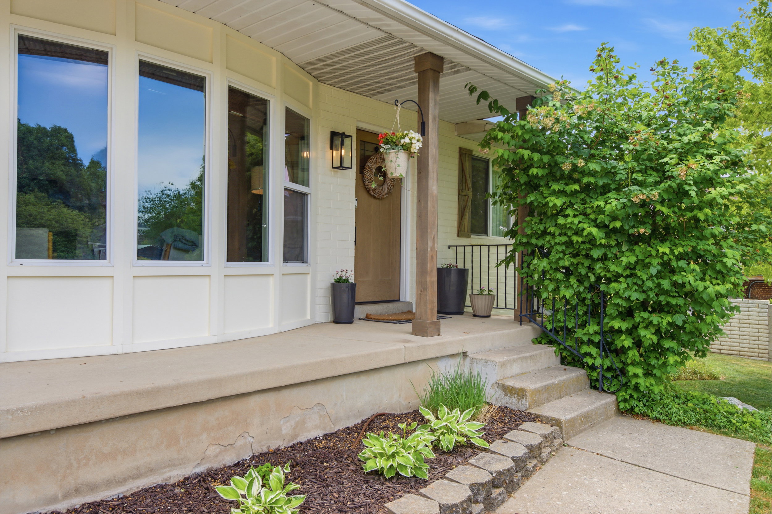 Front entry featuring a covered porch with a wood-finish column, a concrete walkway, and an ornamental shrub