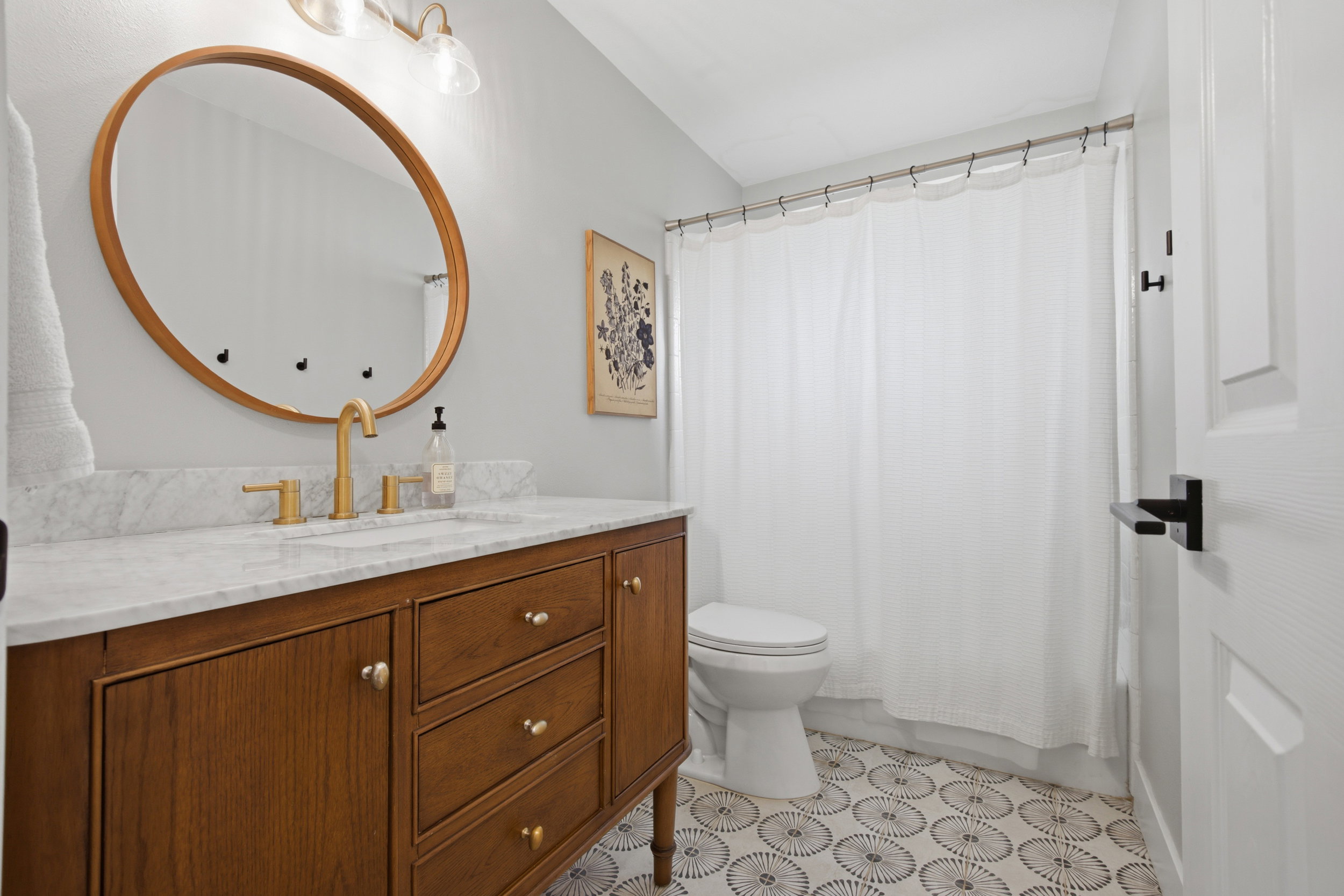 Bathroom featuring a wood-finish vanity with a light countertop, brass-tone fixtures, and a circular mirror