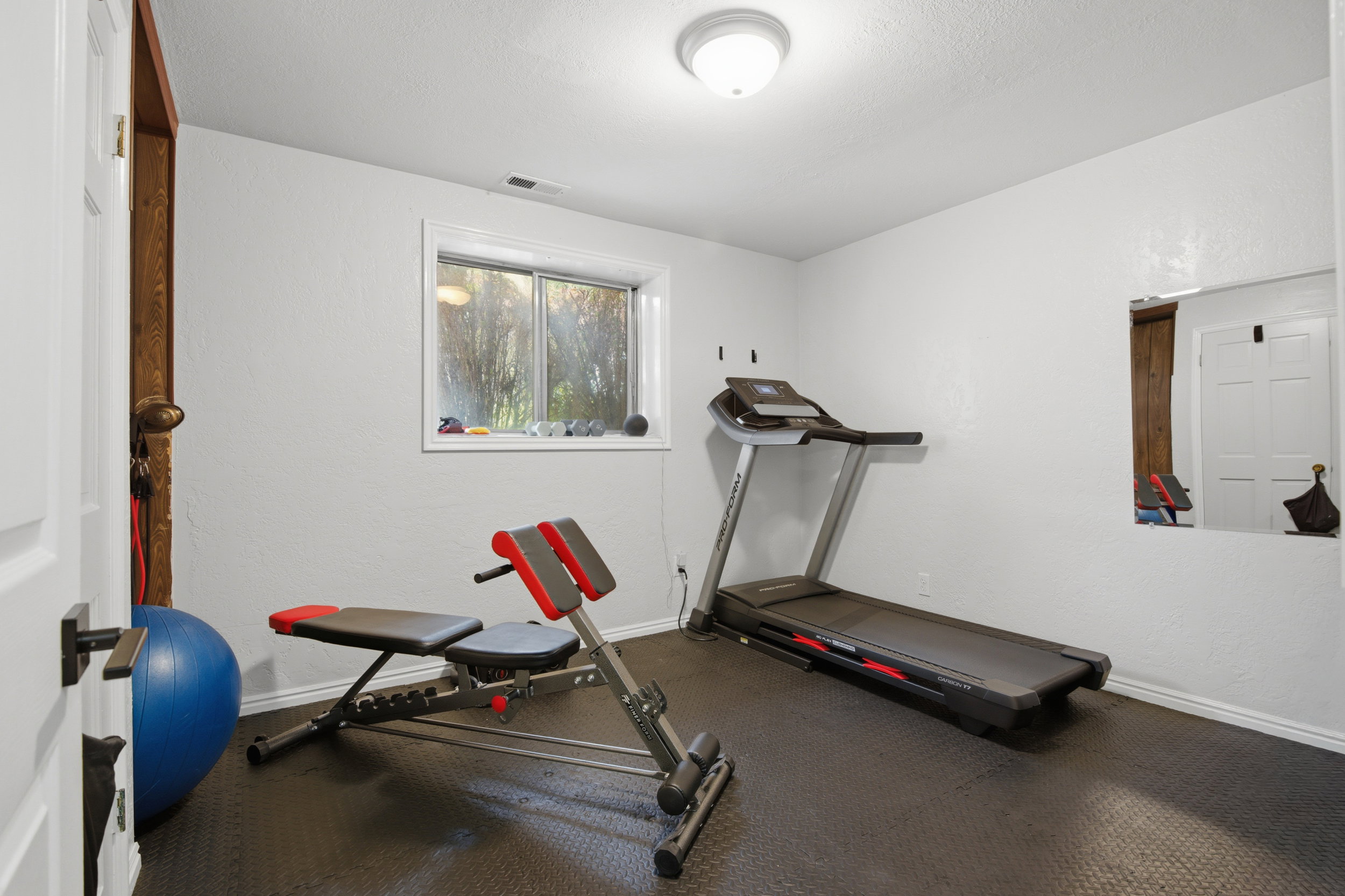 Dedicated exercise room featuring a ground-level window, wall-mounted mirror, overhead lighting, and resilient rubber flooring