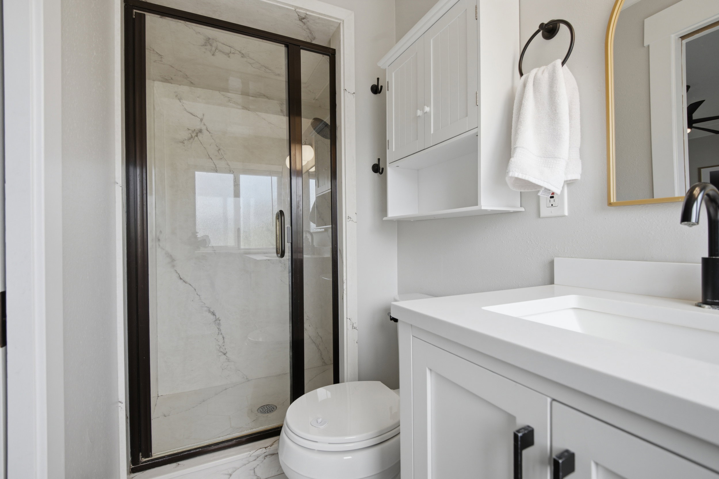 Modern bathroom featuring a glass-enclosed shower with dark bronze framing and marble-look tile surround