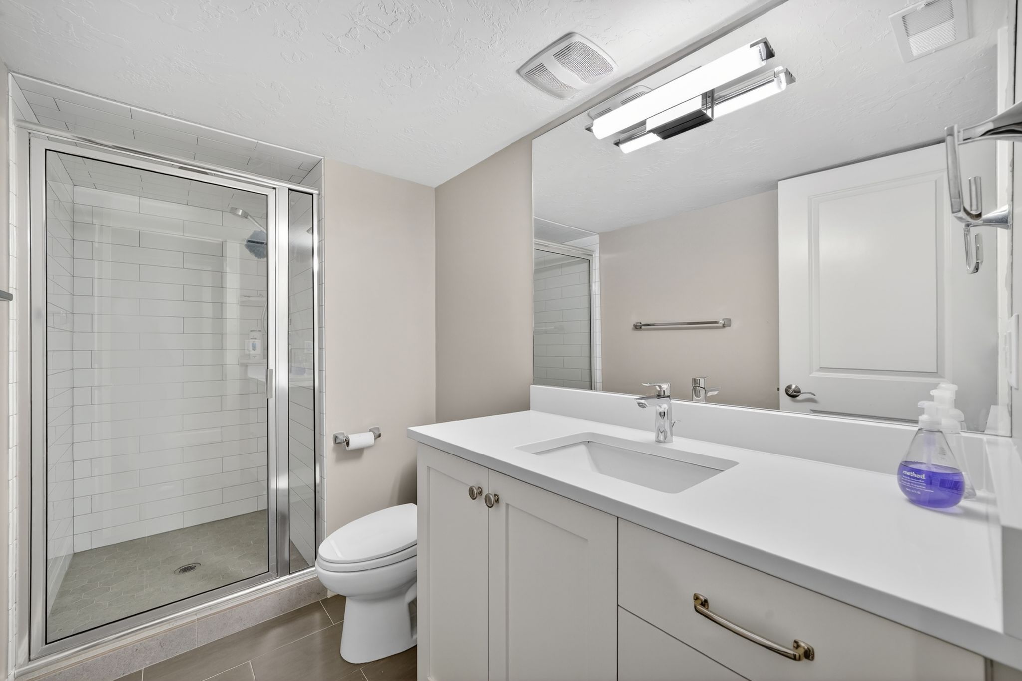 Bathroom featuring a glass-enclosed shower with subway tile surround, white vanity with integrated sink, modern chrome faucet, and expansive wall-mounted mirror