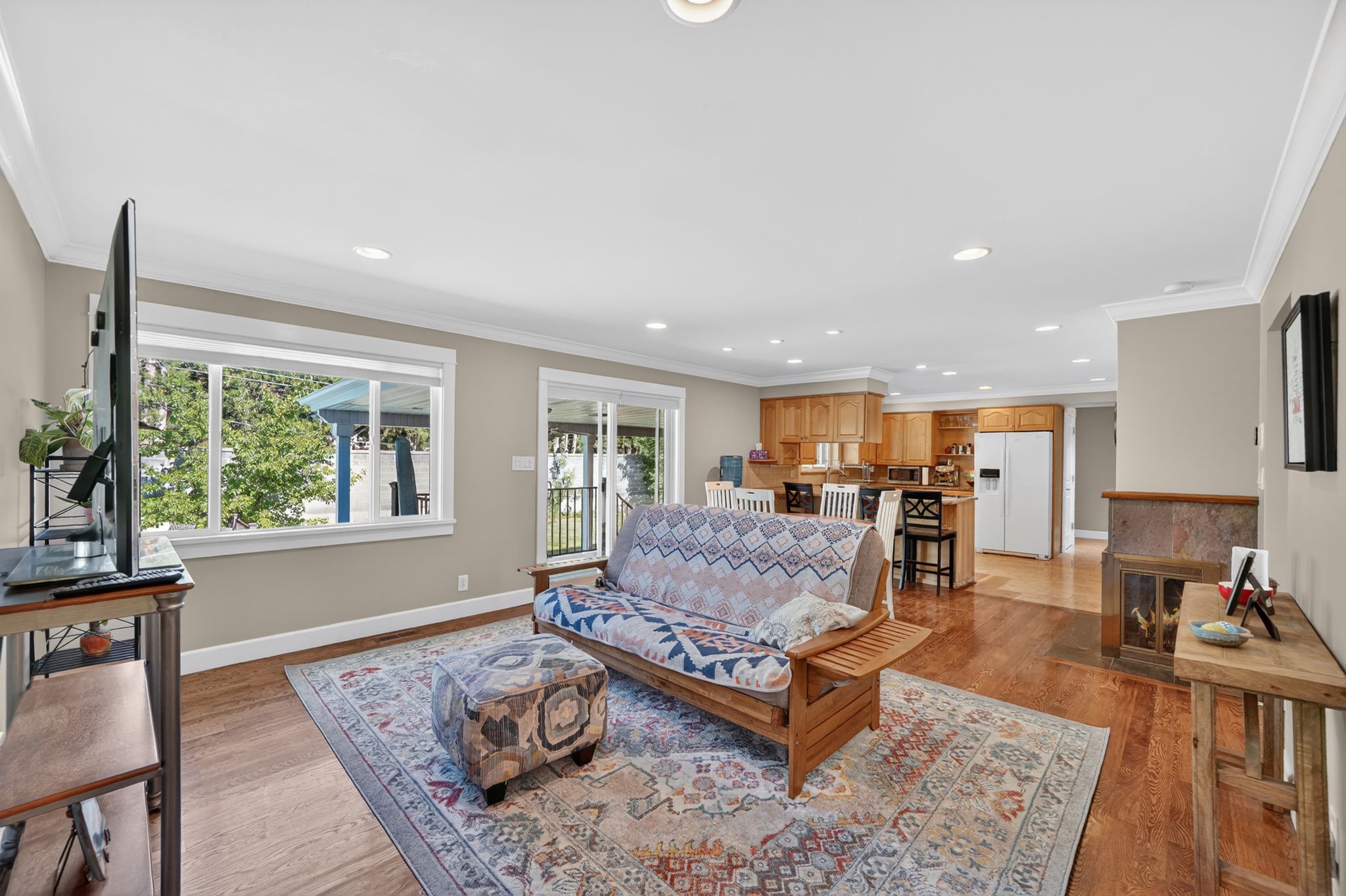 Open-concept living area featuring rich wood-finish flooring, recessed lighting, and a stone-clad fireplace